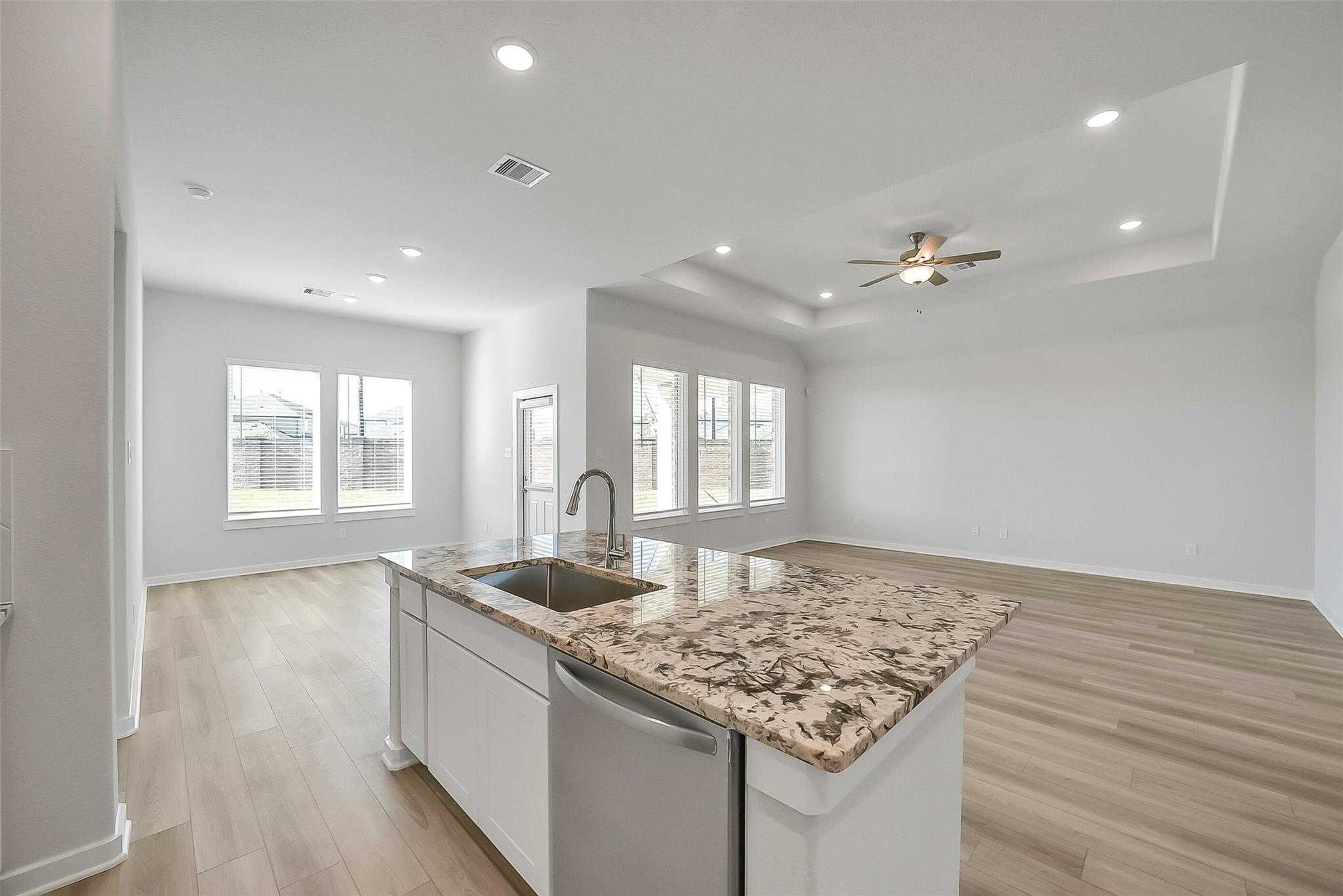 Modern open-concept kitchen featuring granite island, stainless sink, and white cabinets in The Acadia A floor plan, Katy, Texas