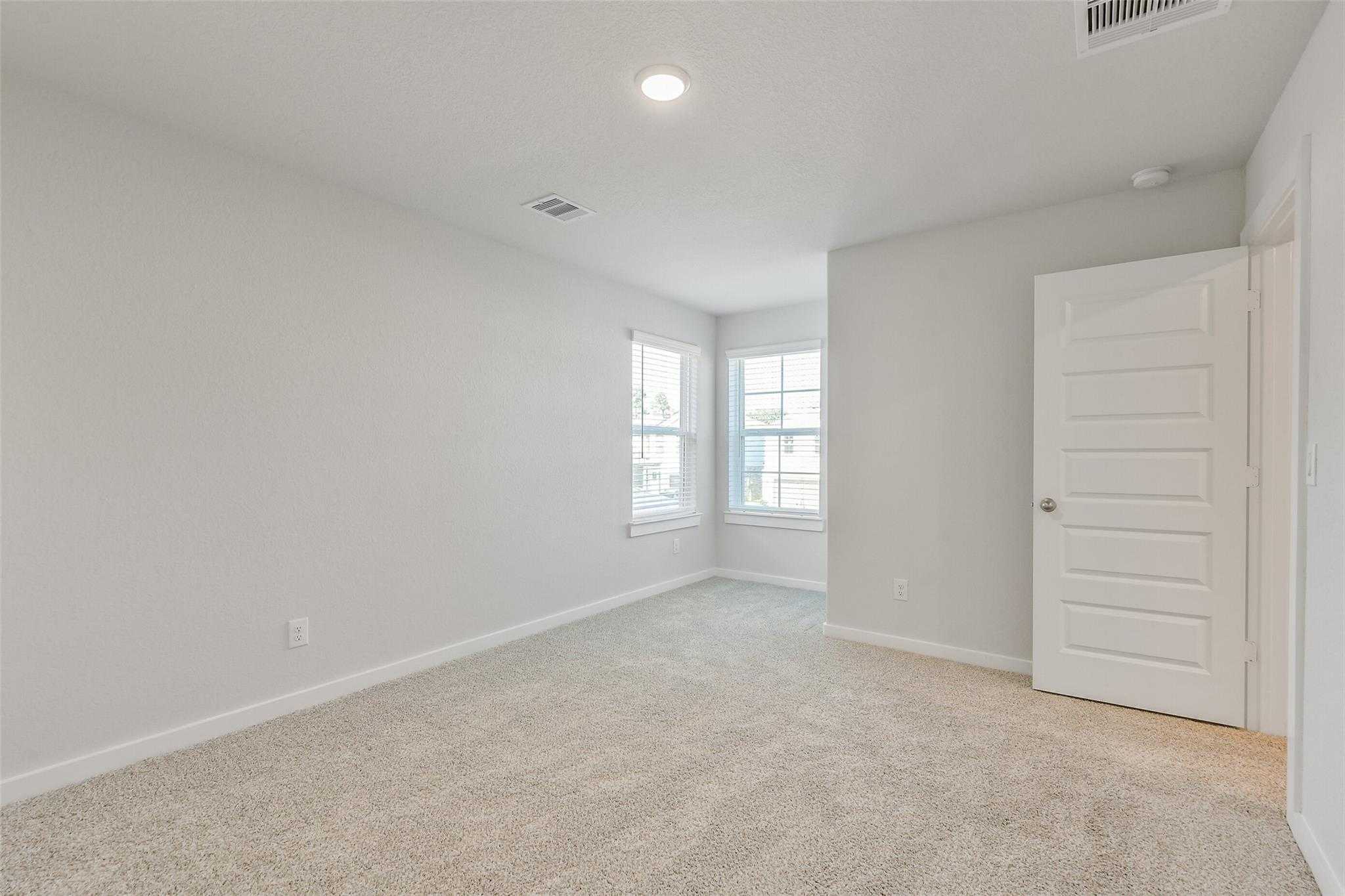 Bright empty bedroom with beige carpet, large windows, and white door in Davidson Homes The Rio Grande H, Magnolia, Texas