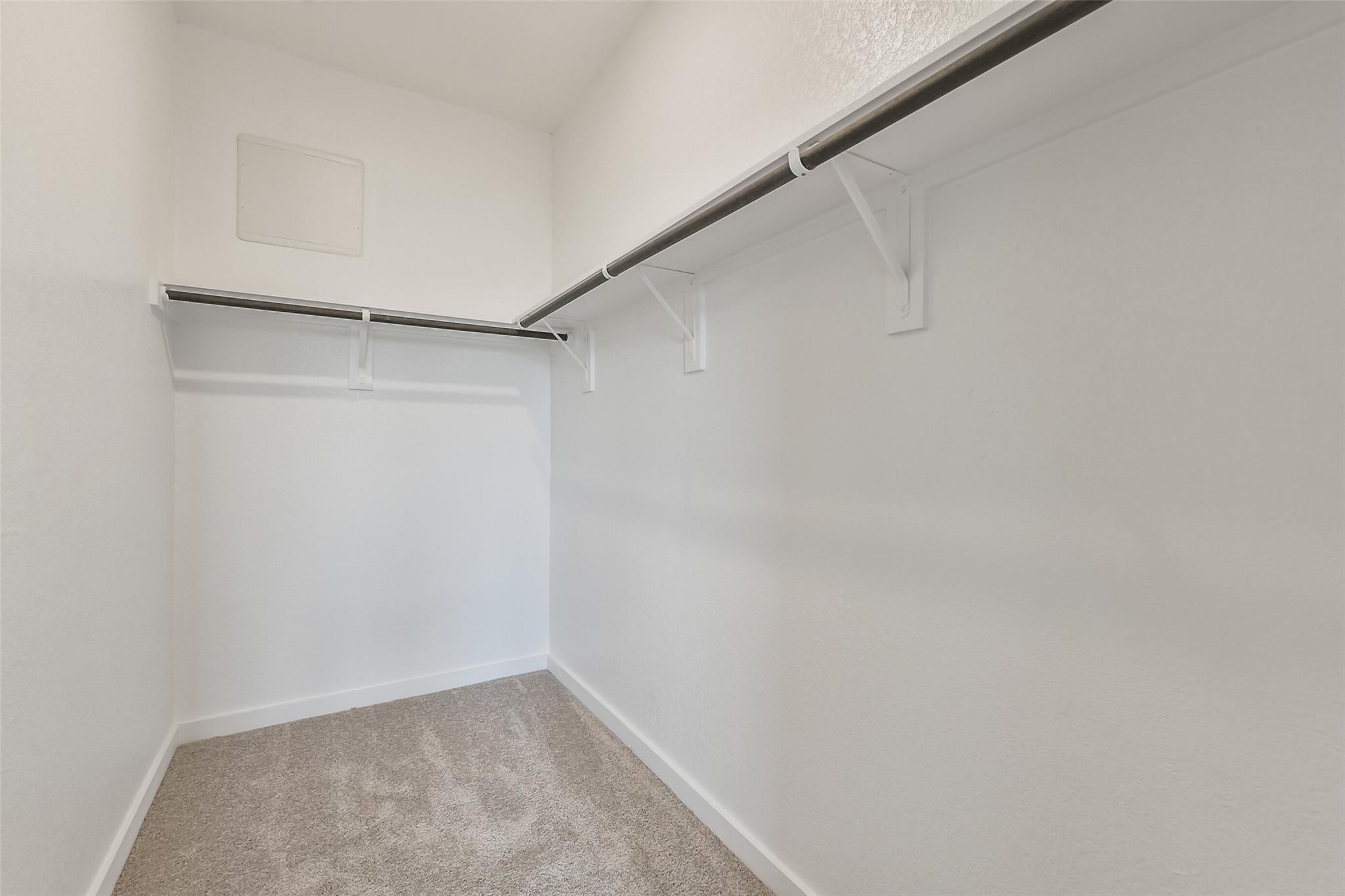 Spacious walk-in closet with double hanging rods, white walls, and carpet floor in Davidson Homes The Frio G, Cleveland, Texas