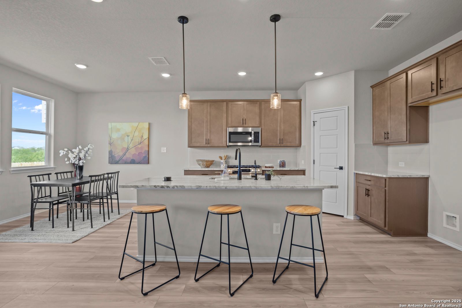 Open-concept kitchen with large granite island, shaker cabinets, pendant lights, and dining nook in The Asheville H, Converse TX