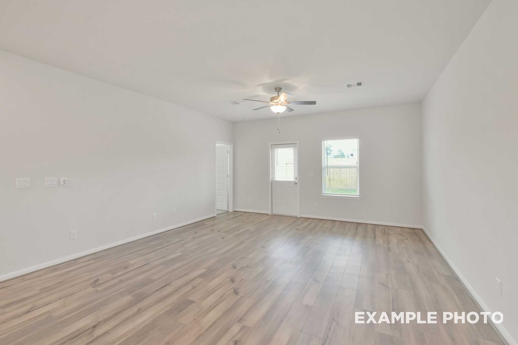 Bright open-concept living area in The Brazos by Davidson Homes, featuring wood-look flooring, ceiling fan, and backyard access door.