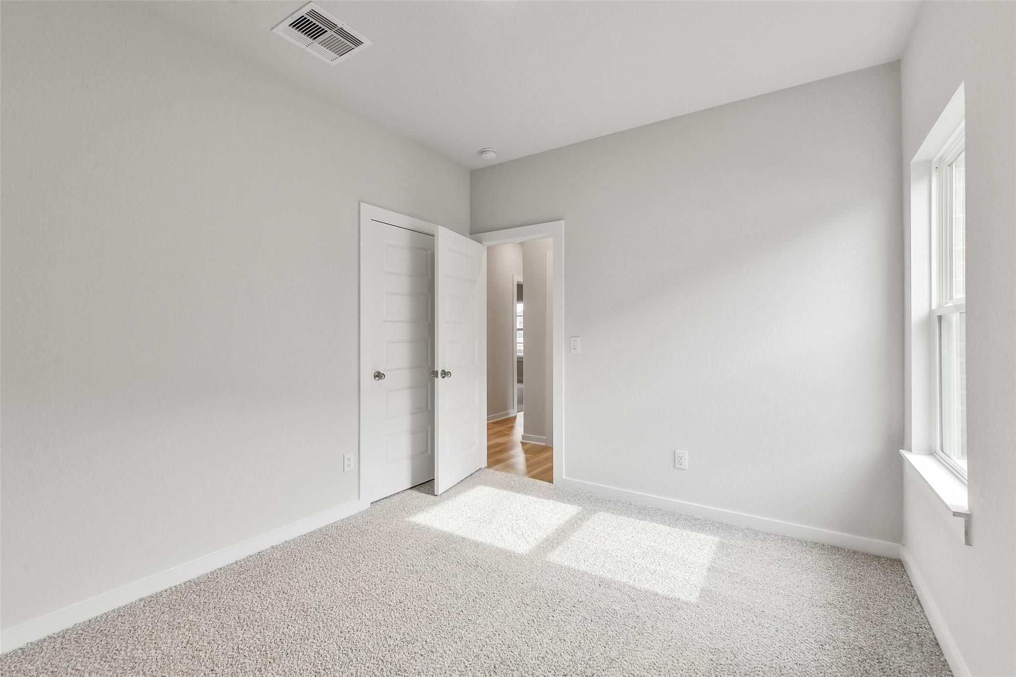 Bright empty bedroom with light gray walls, beige carpet, white doors, and natural sunlight in Davidson Homes The Colorado G, Magnolia TX