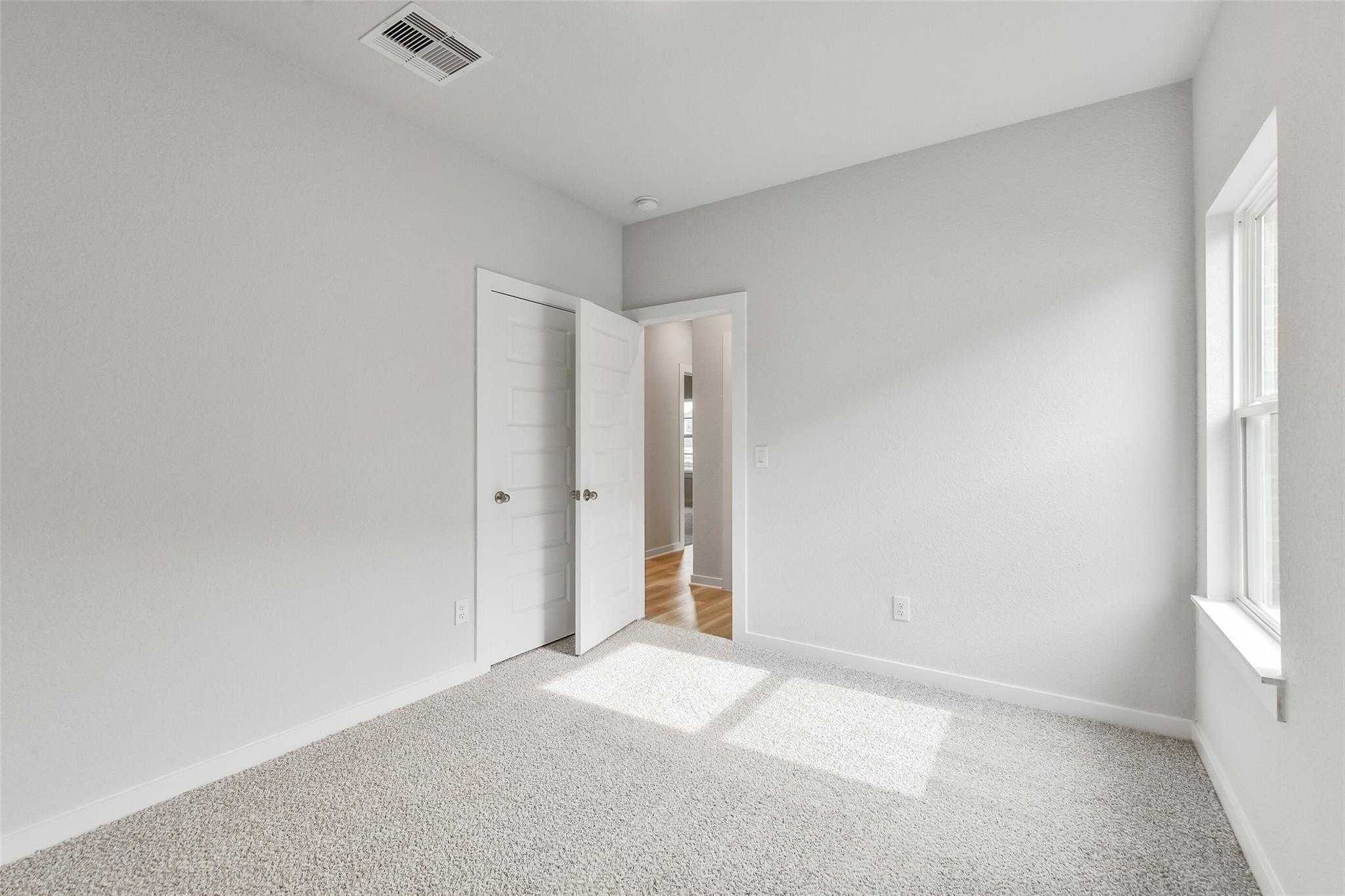 Bright empty bedroom with light gray walls, beige carpet, white doors, and natural sunlight in Davidson Homes The Colorado G, Magnolia TX