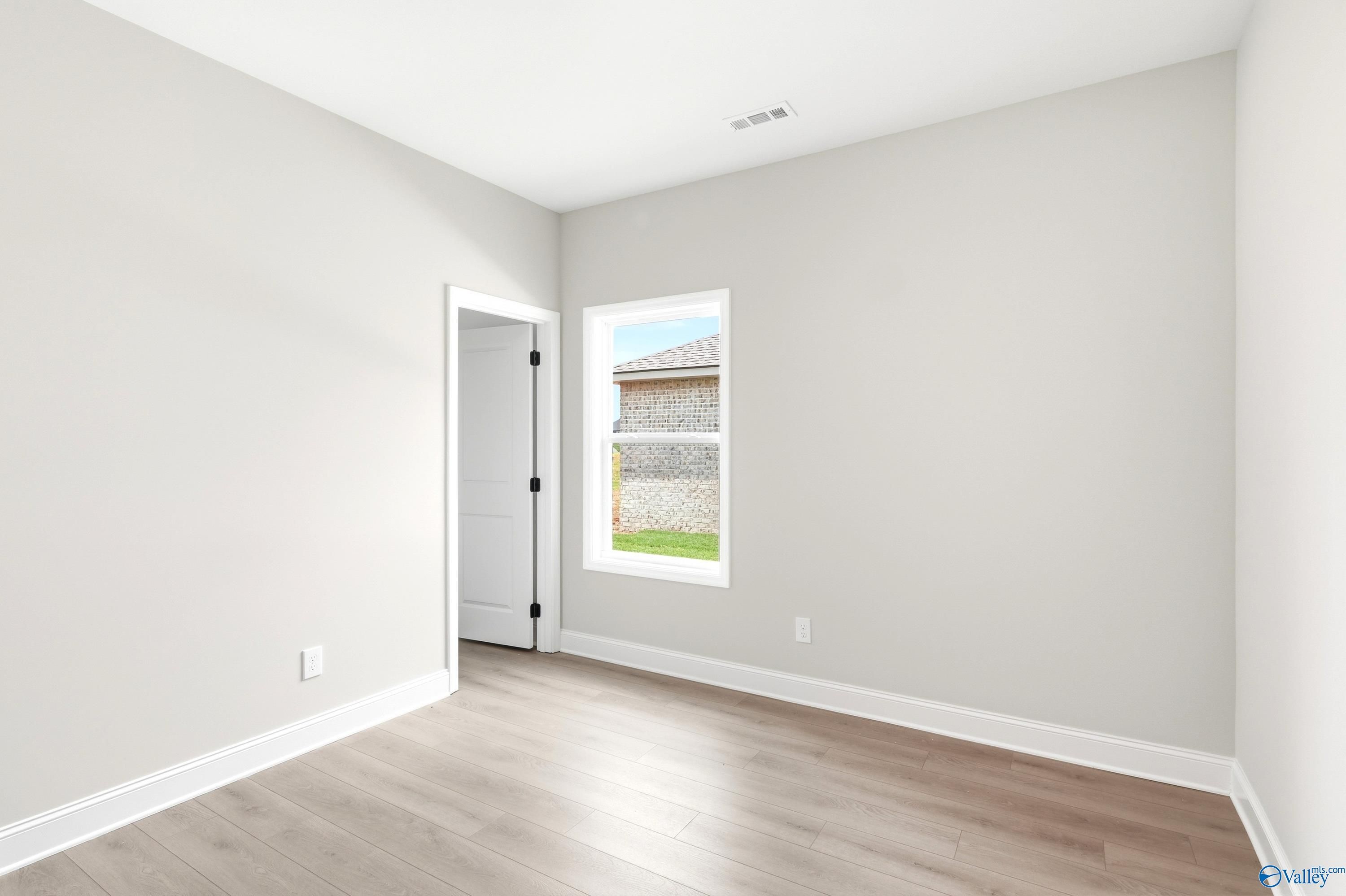 Bright, neutral secondary bedroom with wood-look flooring in The Daphne floor plan at Lynn Meadows, Meridianville, AL.