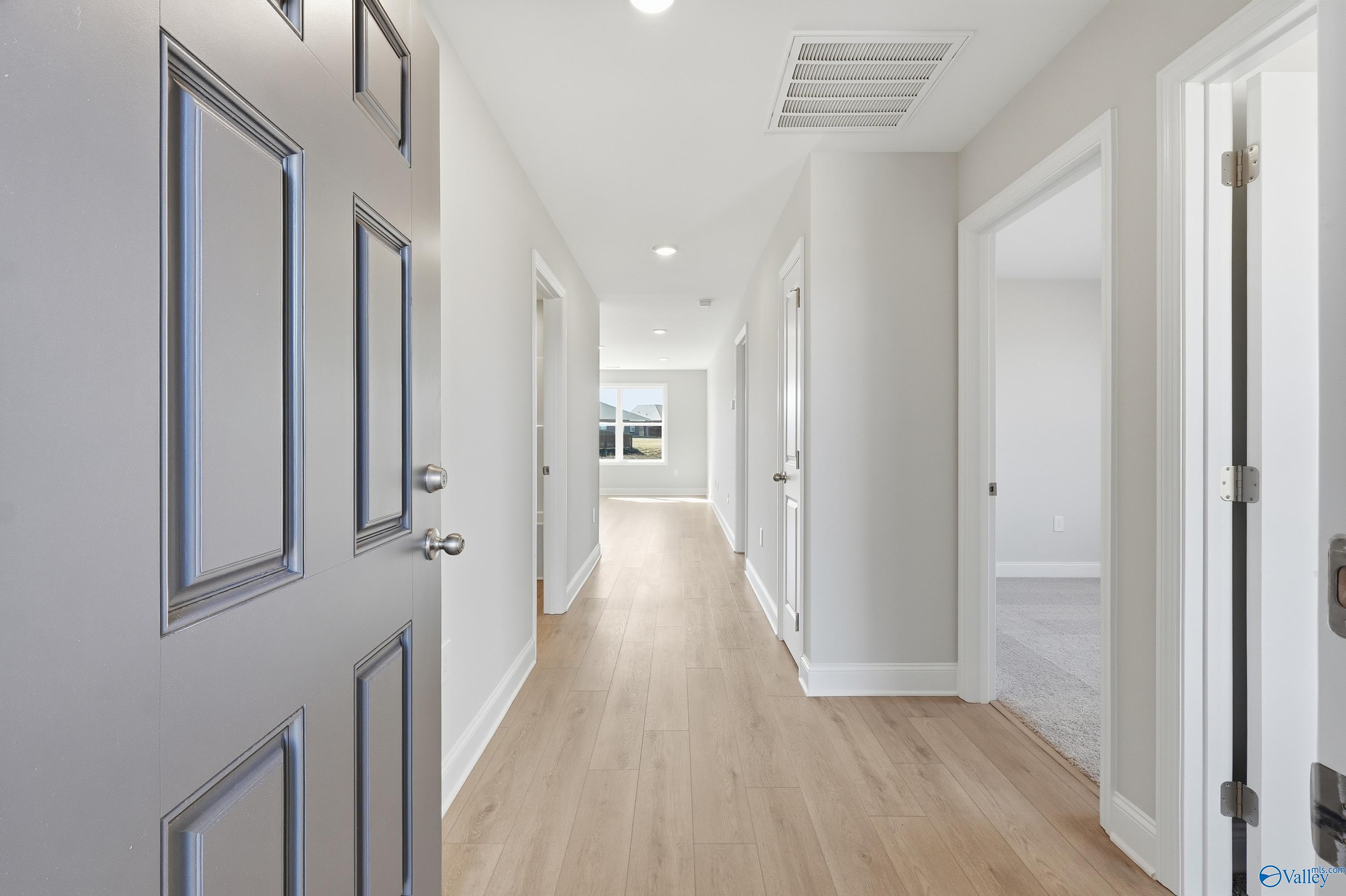 Bright entry hallway with oak hardwood floors, white walls, and open doors in Davidson Homes The Butler, New Market, Alabama