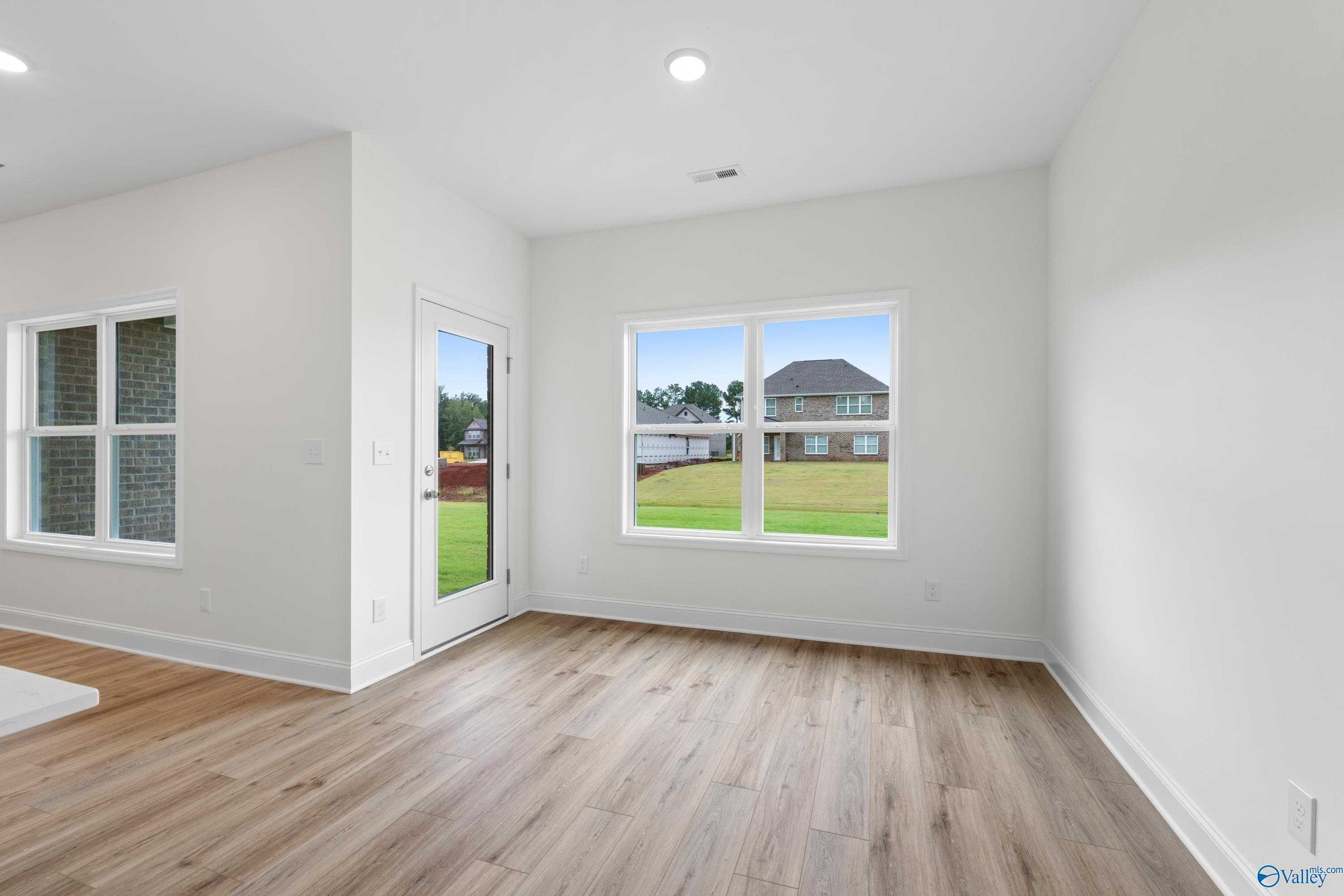 Bright flex room with white walls, hardwood floors, large windows, and glass door to lush backyard in Davidson Homes The Asheville C, Athens AL