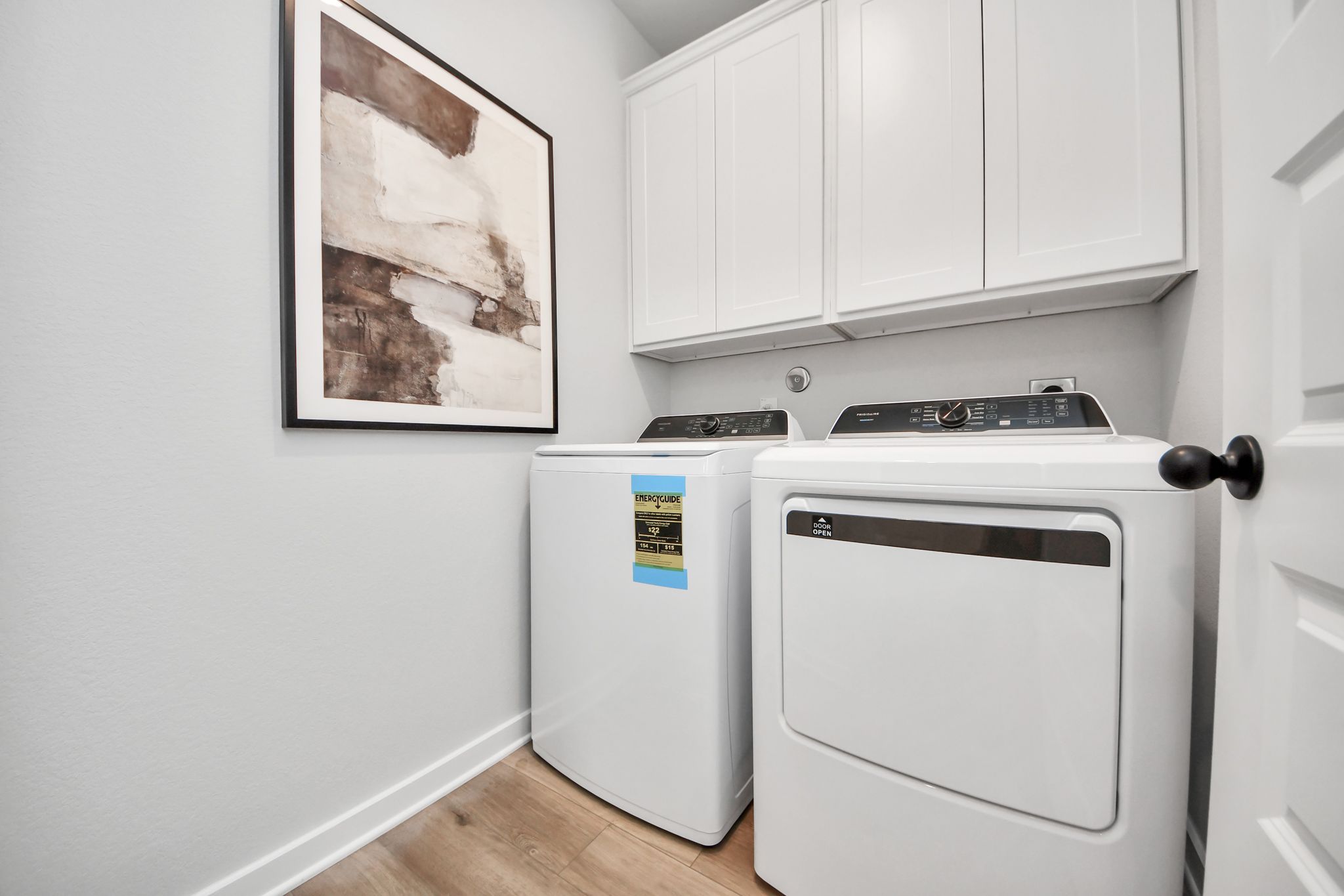 Laundry room at Robins Landing in Houston, TX featuring white cabinetry, modern appliances, and wood-look flooring.