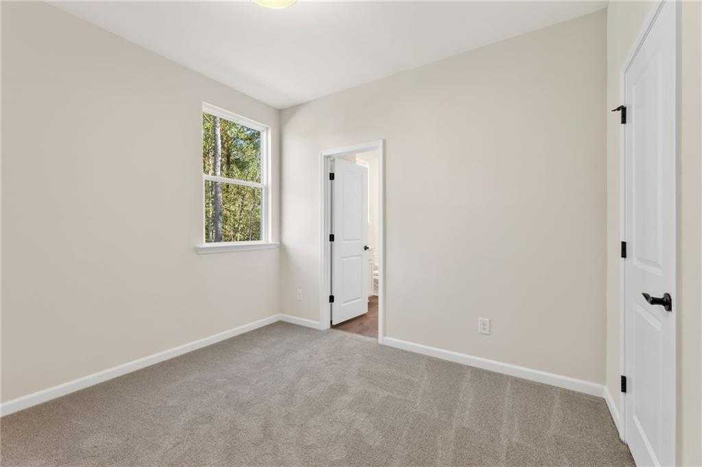 Bright secondary bedroom with beige walls, gray carpet, window blinds, and bath access in The Daphne B, Loganville, GA