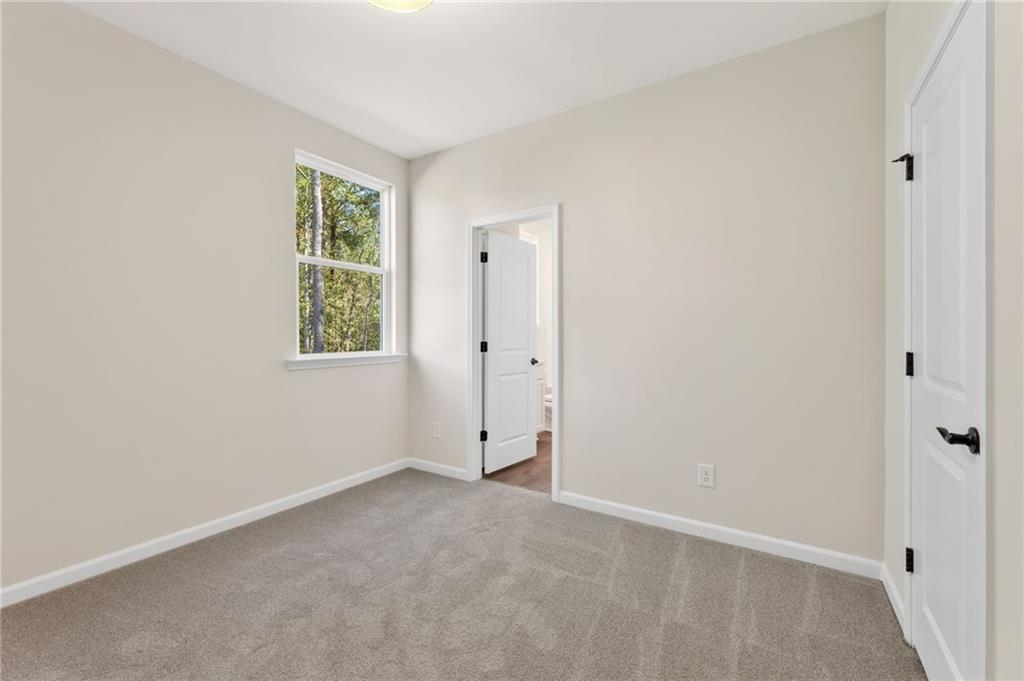 Bright bedroom with beige walls, gray carpet, large window, and en-suite bath door in The Daphne B, Loganville, Georgia