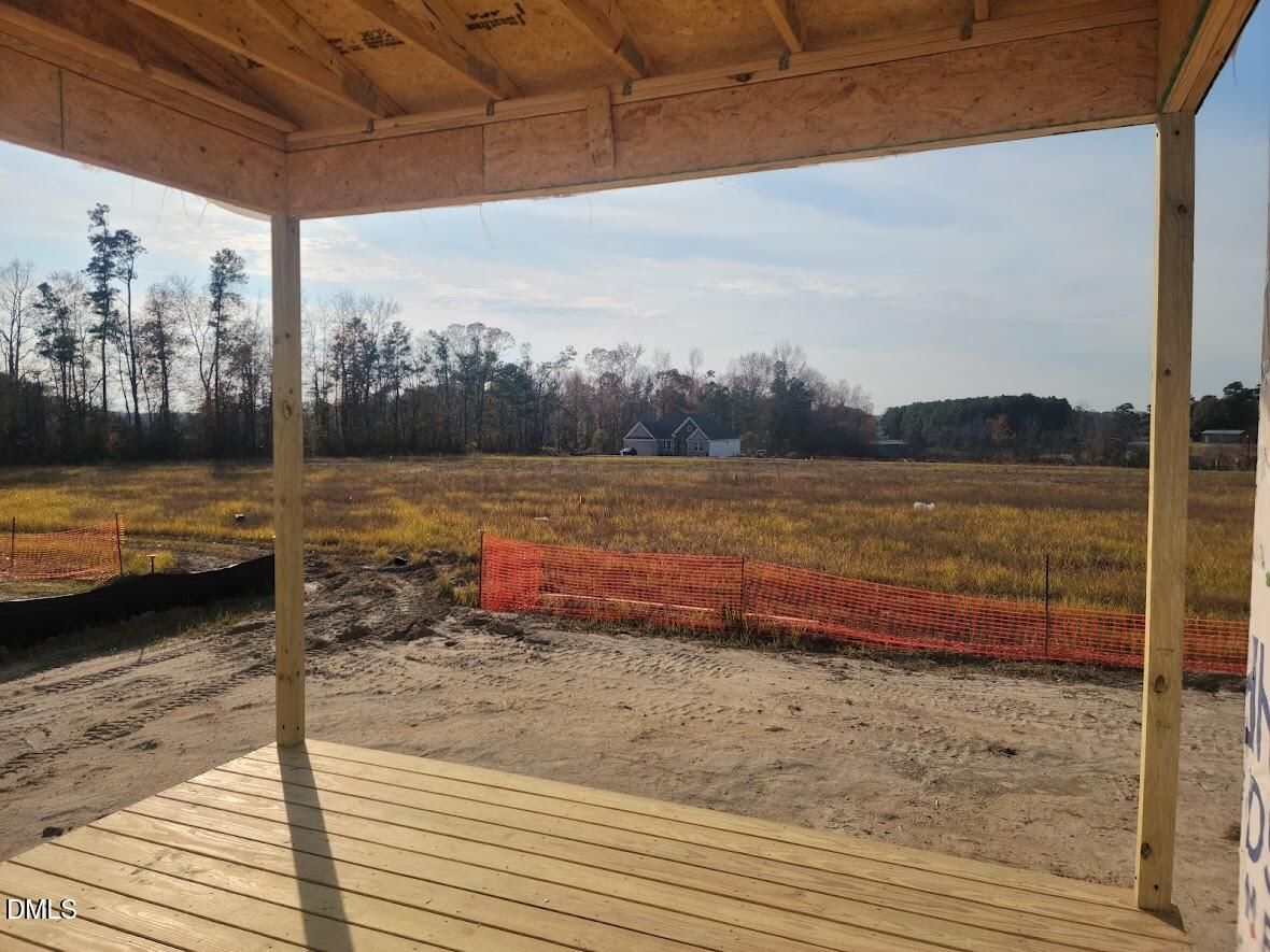 Unfinished wooden porch frame overlooking open field, orange safety fencing, and autumn trees in Tobacco Road, Angier, North Carolina