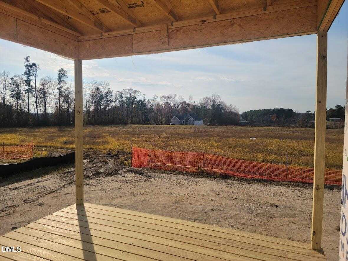Covered wooden deck framing under construction overlooking expansive field with orange fencing and autumn trees in Angier, North Carolina