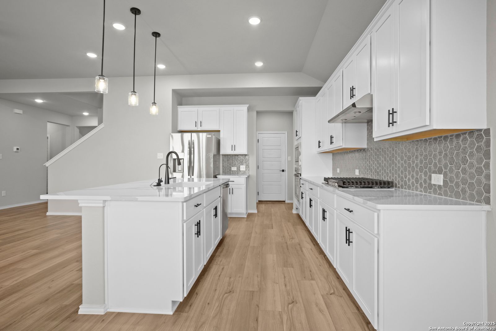Modern white kitchen with large island, stainless appliances, geometric tile backsplash in The Sequoia A, Converse, Texas