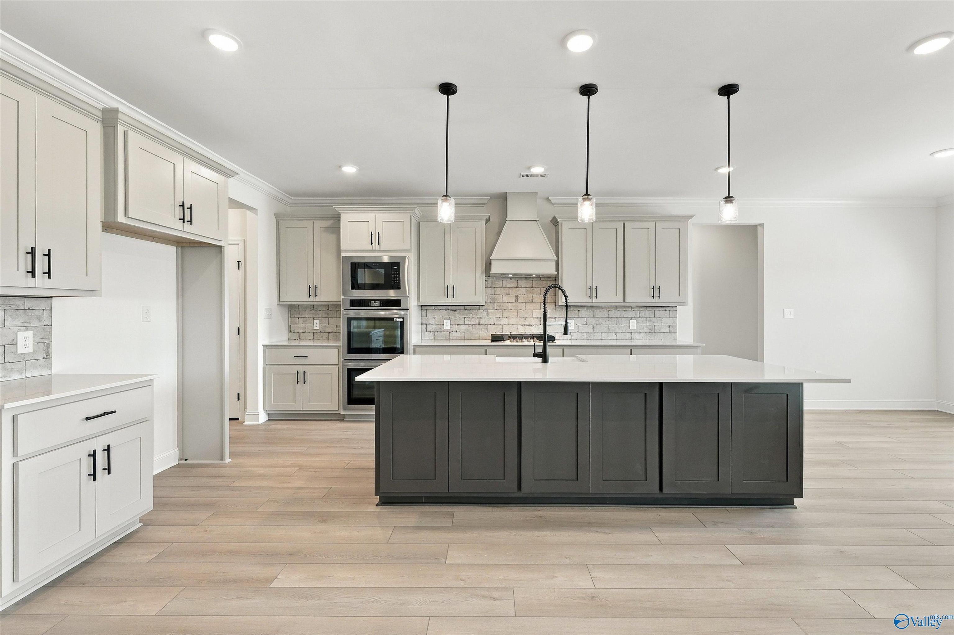Modern kitchen with gray island, white cabinetry, pendant lights, and stainless appliances in Davidson Homes The Valencia, Huntsville