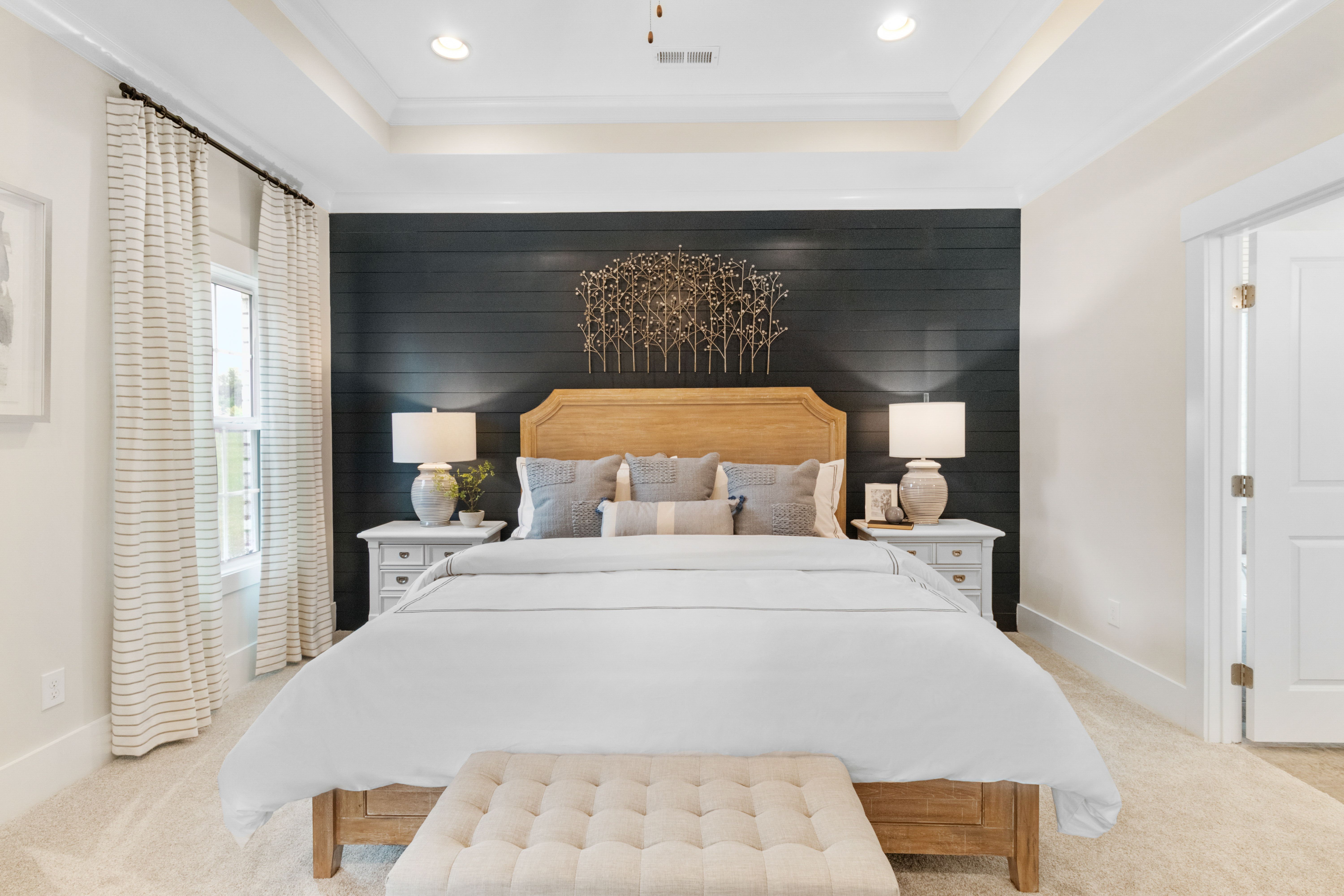 Spacious master bedroom at Noble Ridge in Cullman Alabama featuring king bed with white linens, black shiplap accent wall, and bedside lamps