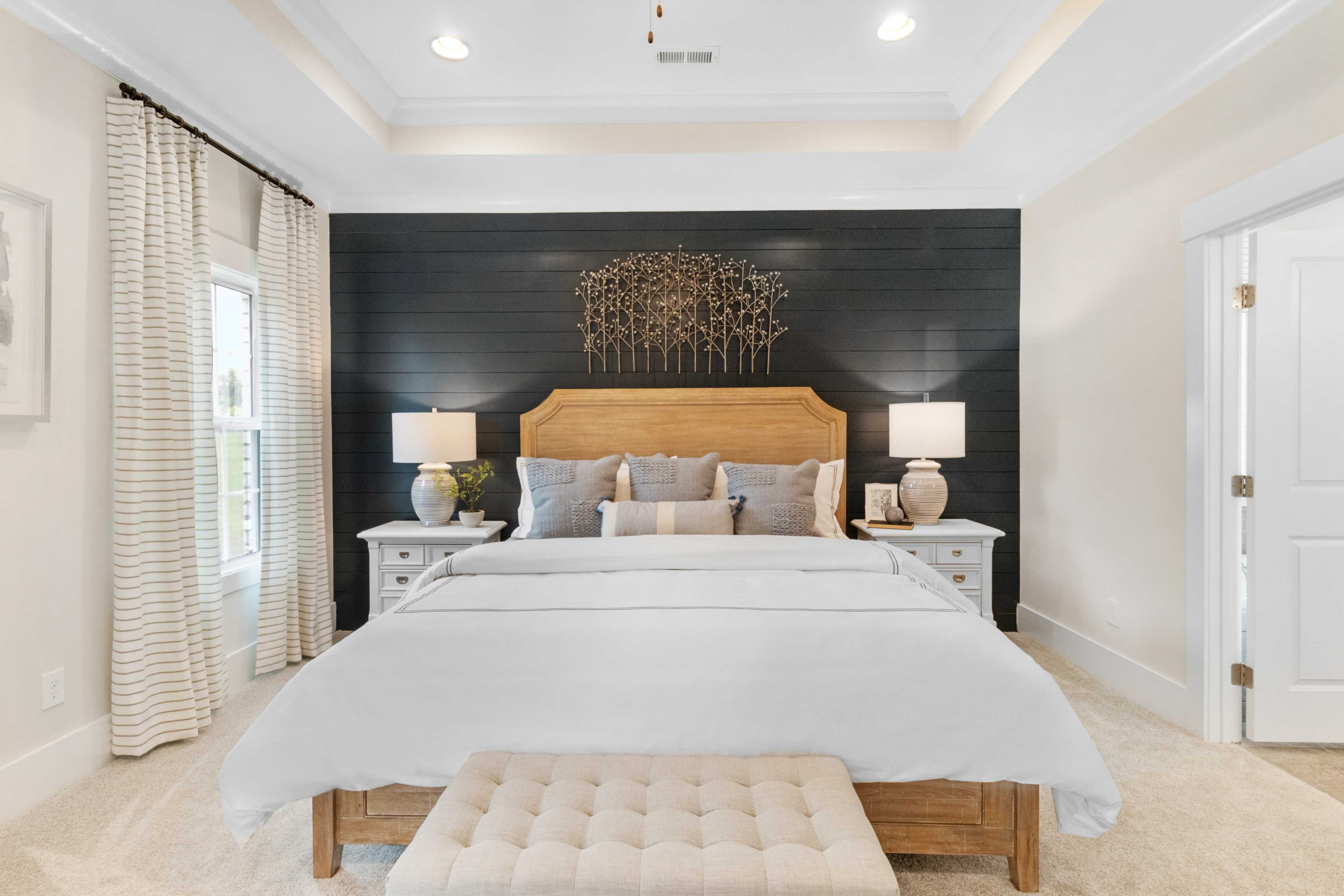 Spacious master bedroom at Noble Ridge in Cullman Alabama featuring king bed with white linens, black shiplap accent wall, and bedside lamps