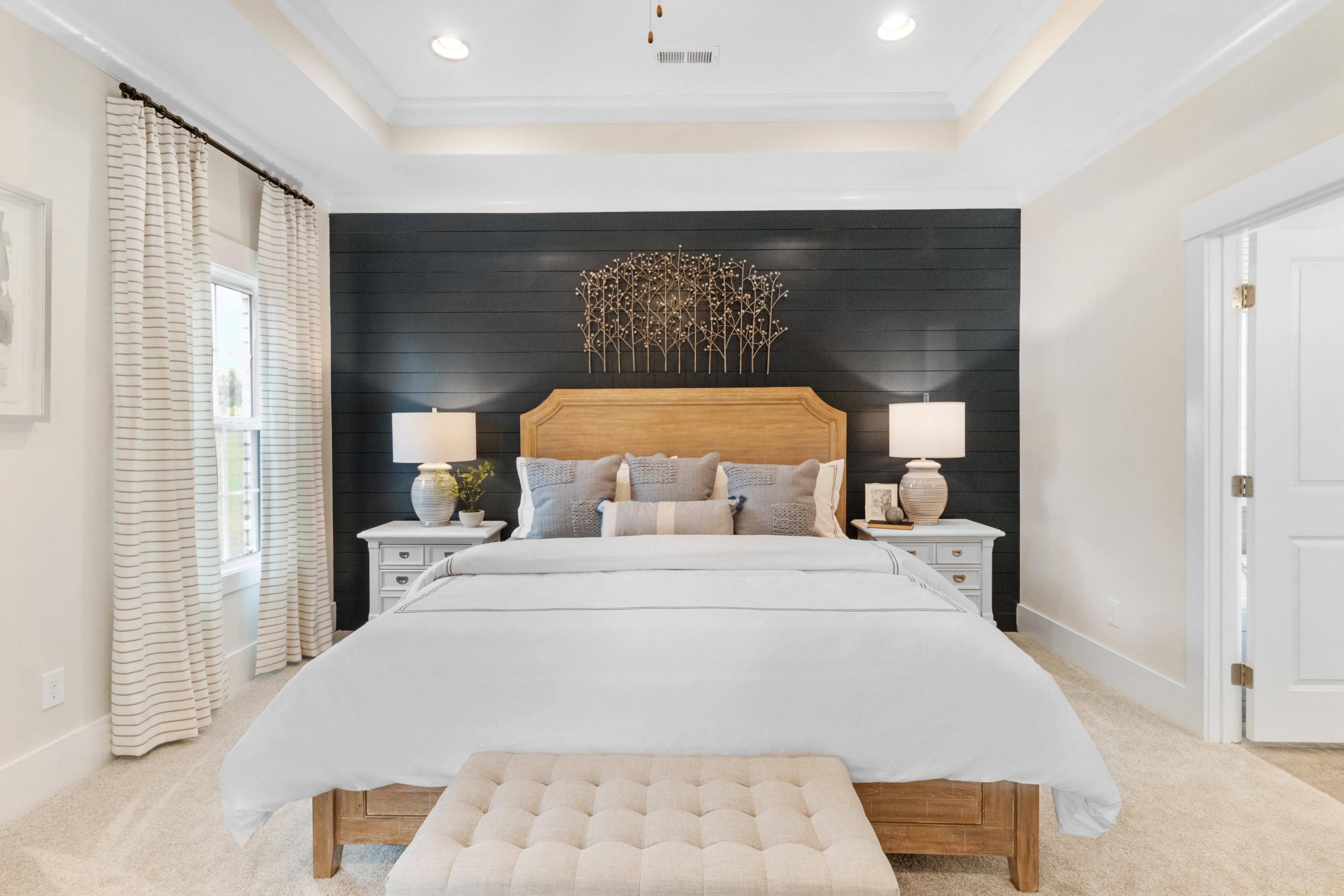 Spacious master bedroom at Noble Ridge in Cullman Alabama featuring king bed with white linens, black shiplap accent wall, and bedside lamps