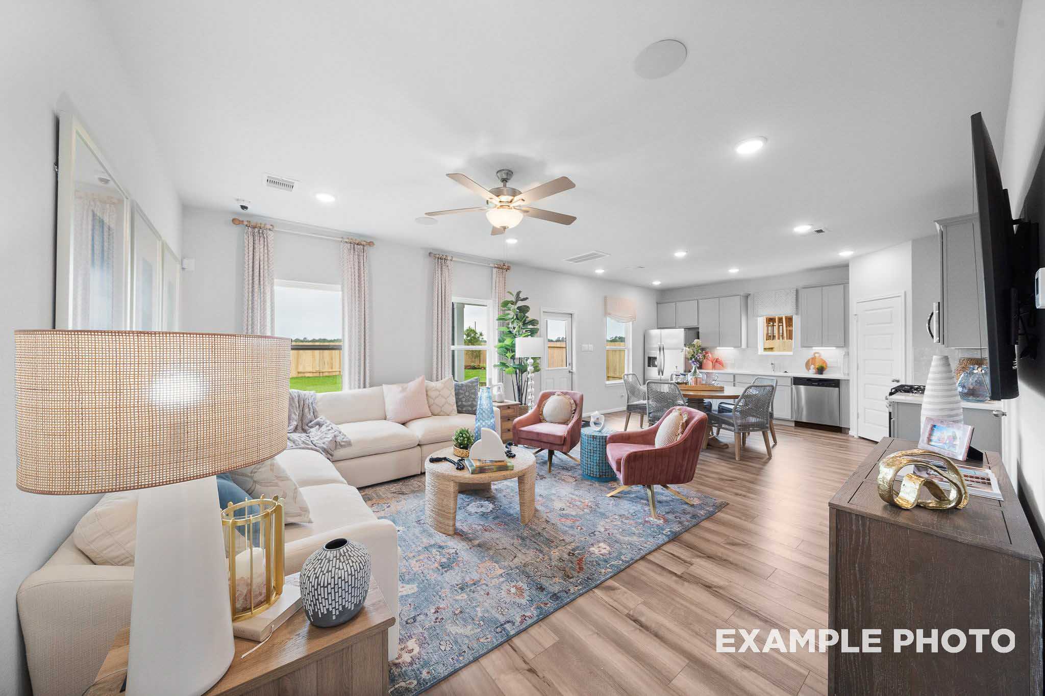 Spacious open-concept living room in The Trinity floor plan featuring white sectional sofa, accent chairs, kitchen island, and large windows