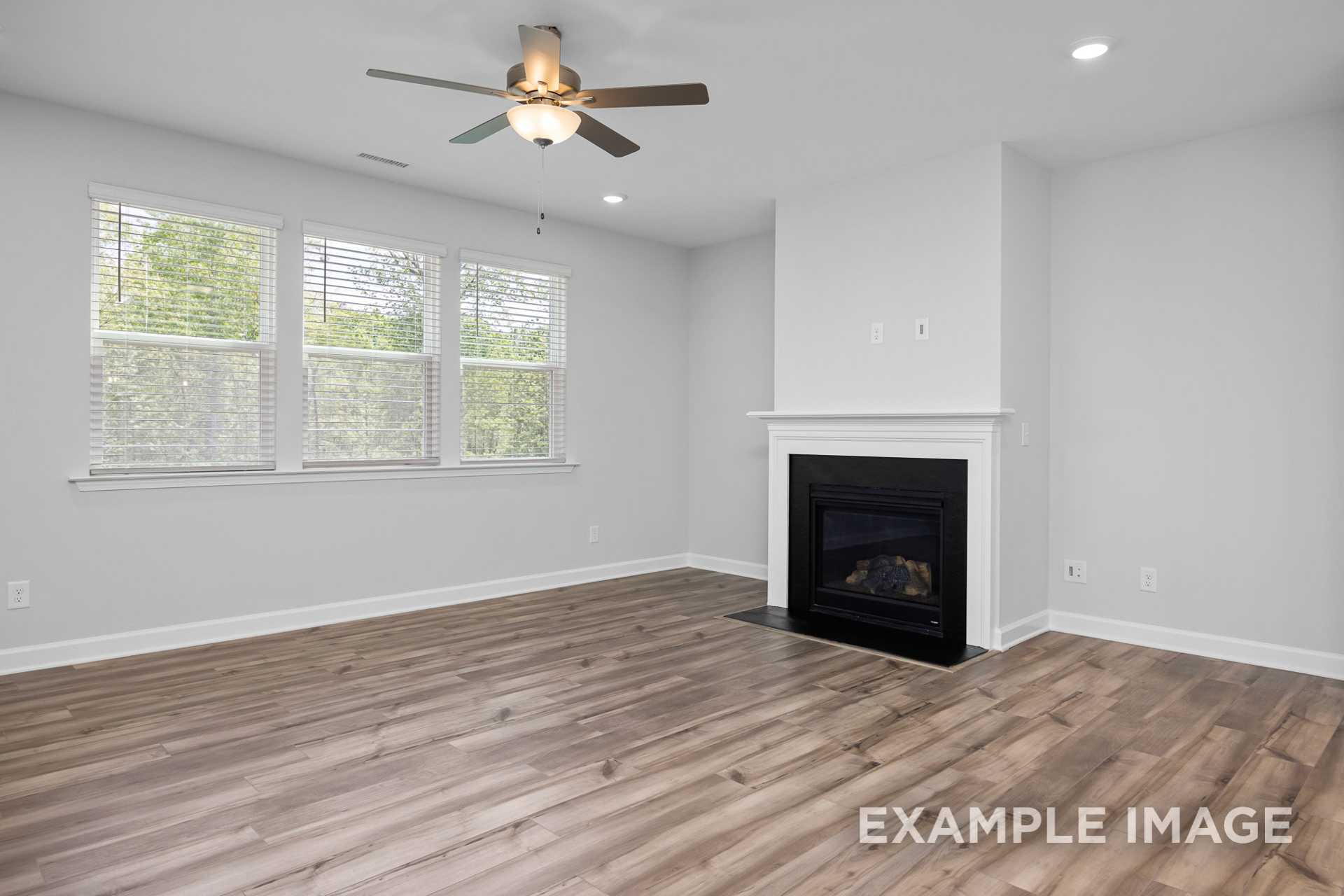 Spacious living room in The Preston B featuring gas fireplace, hardwood floors, ceiling fan, and large windows with natural light