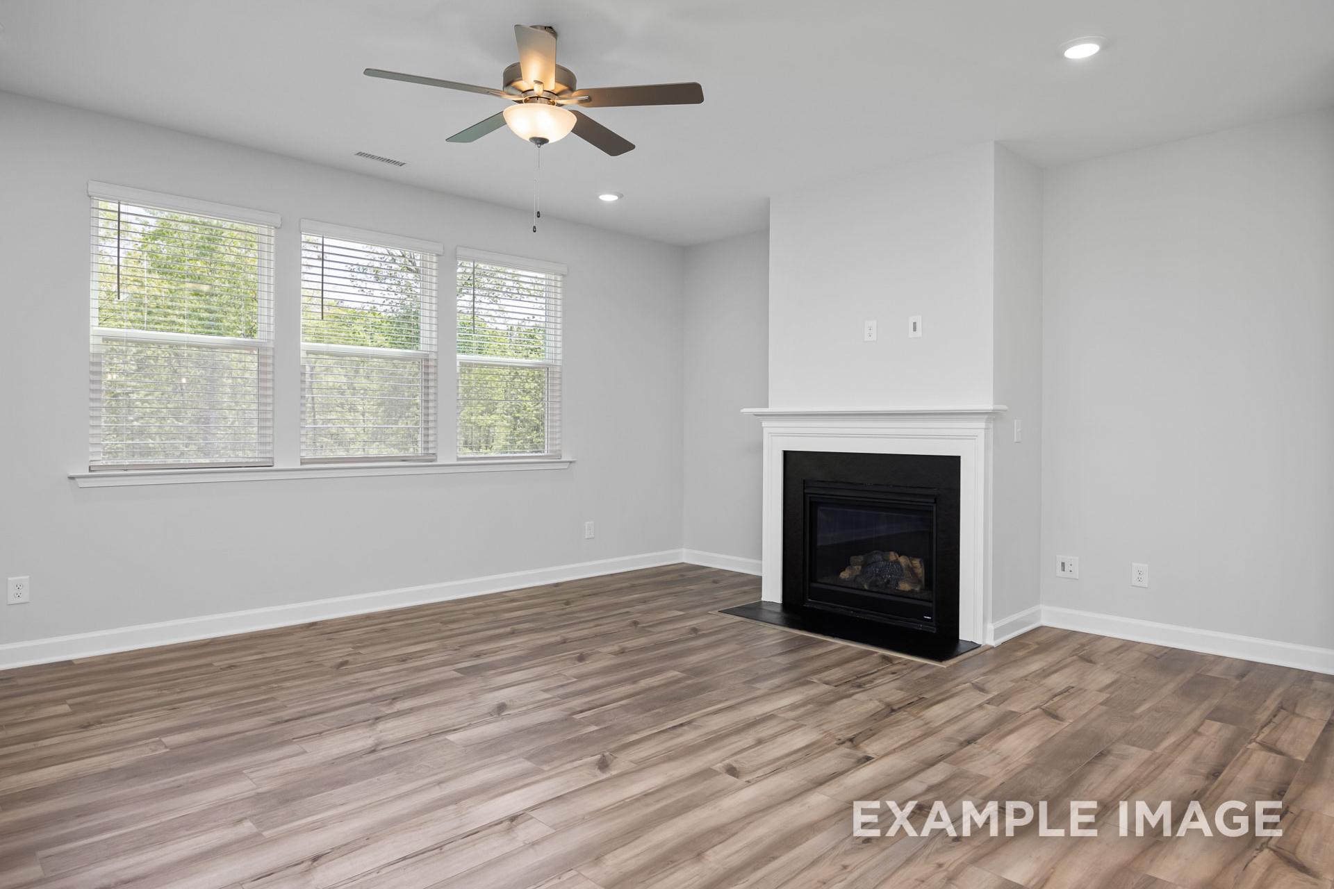 Spacious living room in The Preston B featuring gas fireplace, hardwood floors, ceiling fan, and large windows with natural light