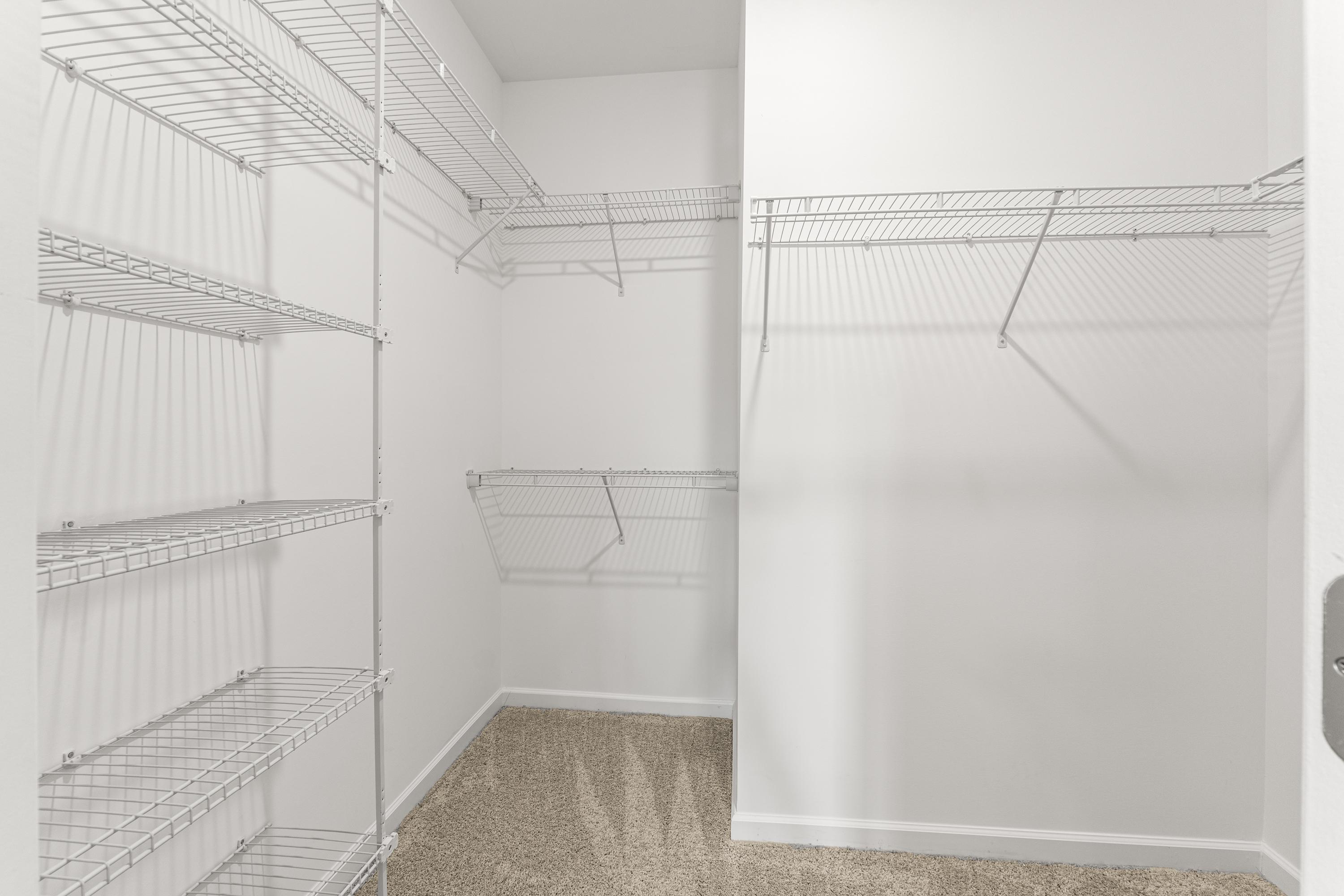 Spacious walk-in closet in The Haven E master suite with white wire shelving, hanging rods, and beige carpet