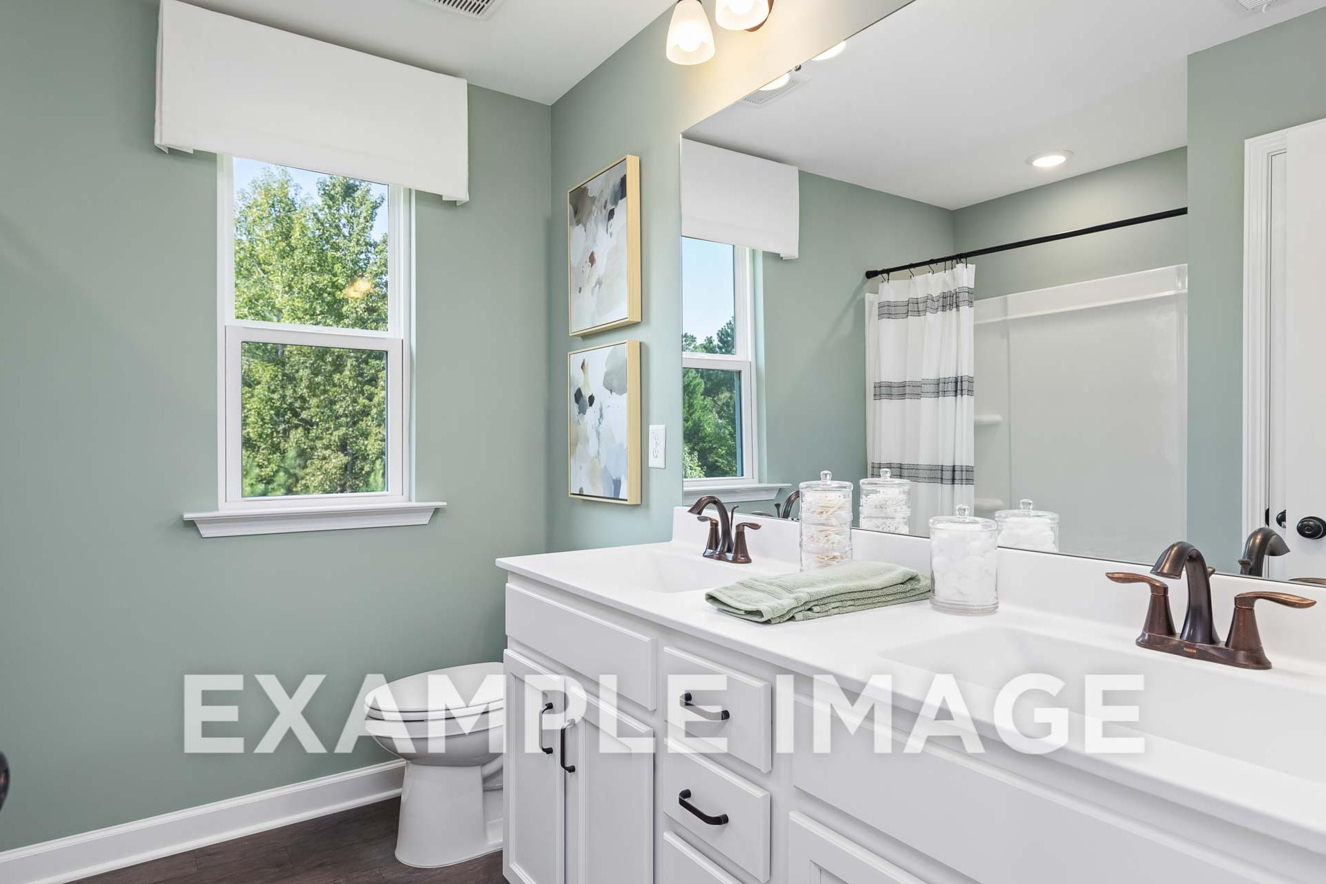 Spacious master bathroom in The Willow E with double vanity, sage green walls, large window, and modern fixtures
