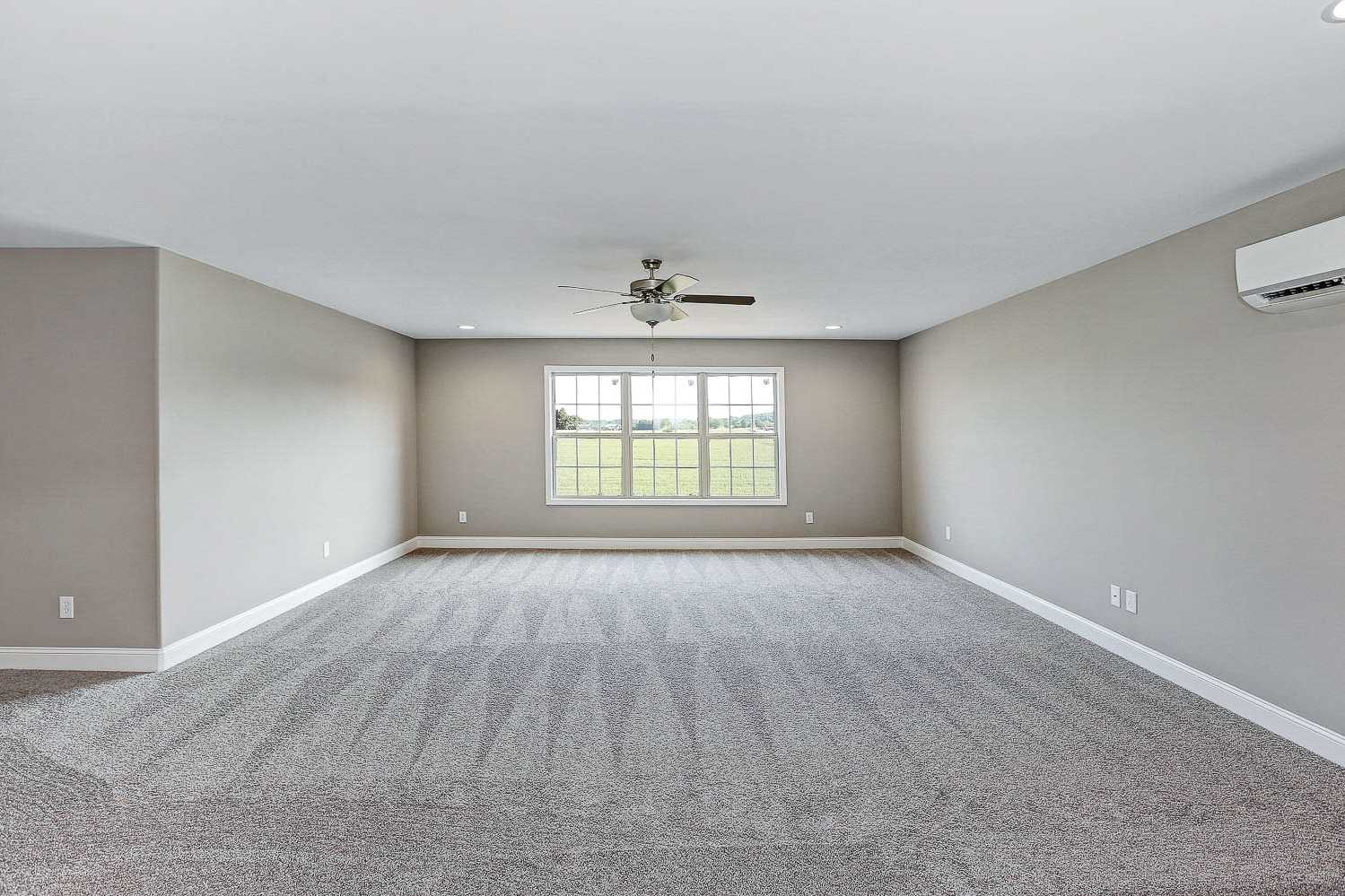 Spacious bonus room in The Montgomery home with gray walls, carpeted floor, ceiling fan, and large window overlooking fields