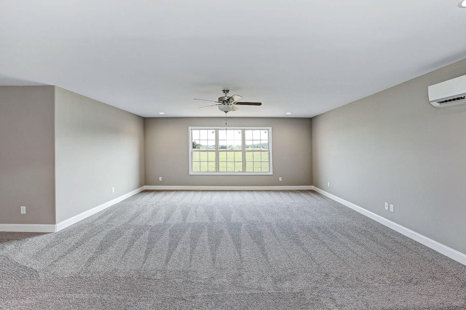 Spacious bonus room in The Montgomery home with gray walls, carpeted floor, ceiling fan, and large window overlooking fields