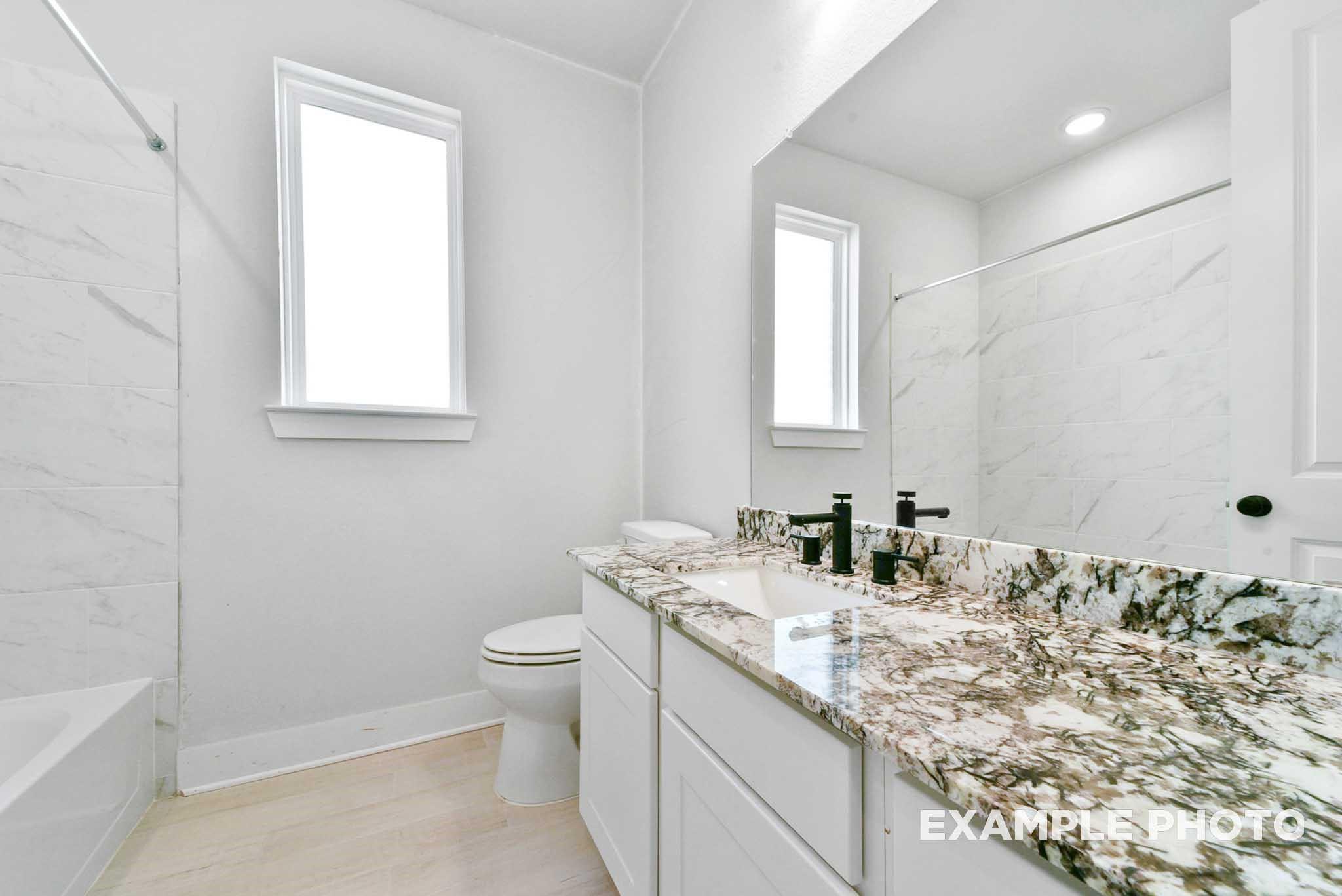 Bright bathroom with white subway tile shower, granite vanity, black faucet, and toilet in Davidson Homes The George A, Texas City