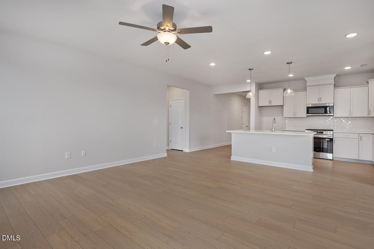 Open-concept kitchen and living area with white cabinets, stainless steel appliances, ceiling fan, and hardwood floors in Davidson Homes The Daphne C, Lillington, NC