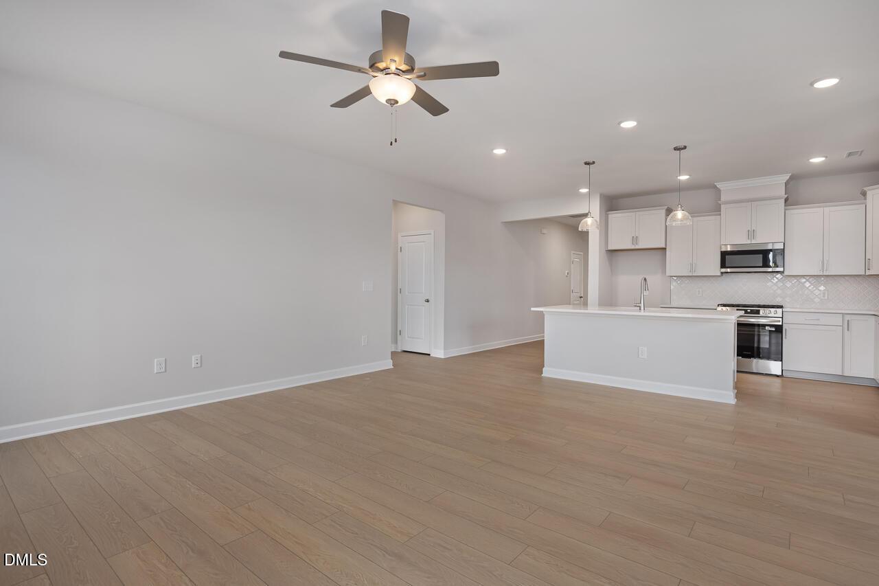 Open-concept kitchen and living area with white cabinets, stainless steel appliances, ceiling fan, and hardwood floors in Davidson Homes The Daphne C, Lillington, NC