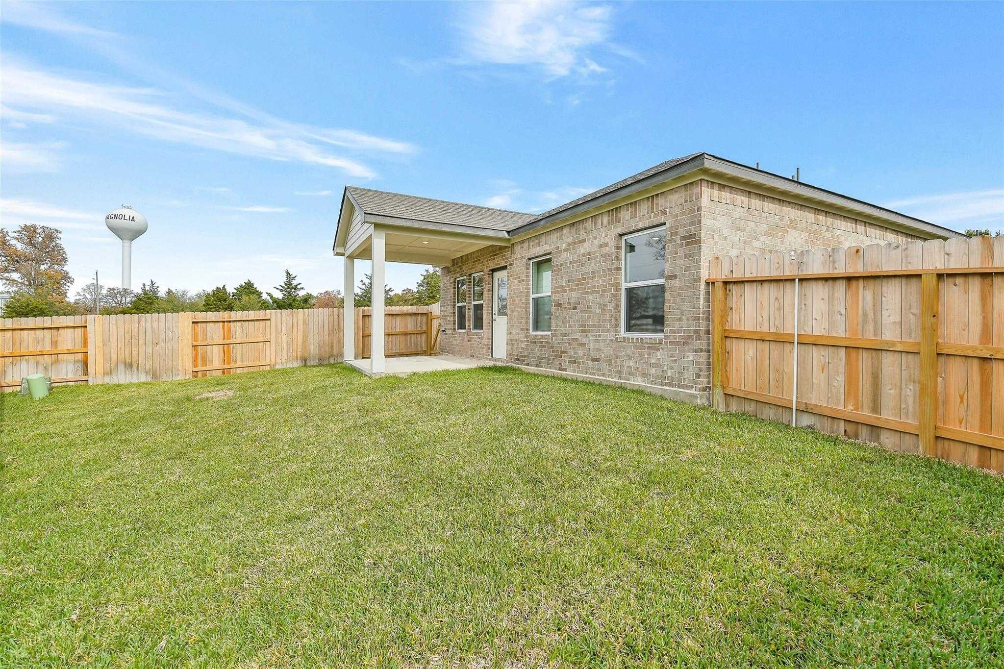 Single-story brick home with covered patio, wooden privacy fence, lush green yard in Windmill Estates, Magnolia, Texas - Davidson Homes Colorado G