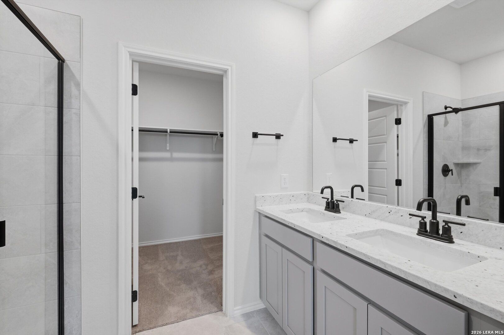 Modern master bath with double quartz vanity, gray cabinets, frameless glass shower, and adjacent walk-in closet in Davidson Homes The Blanco C, San Antonio