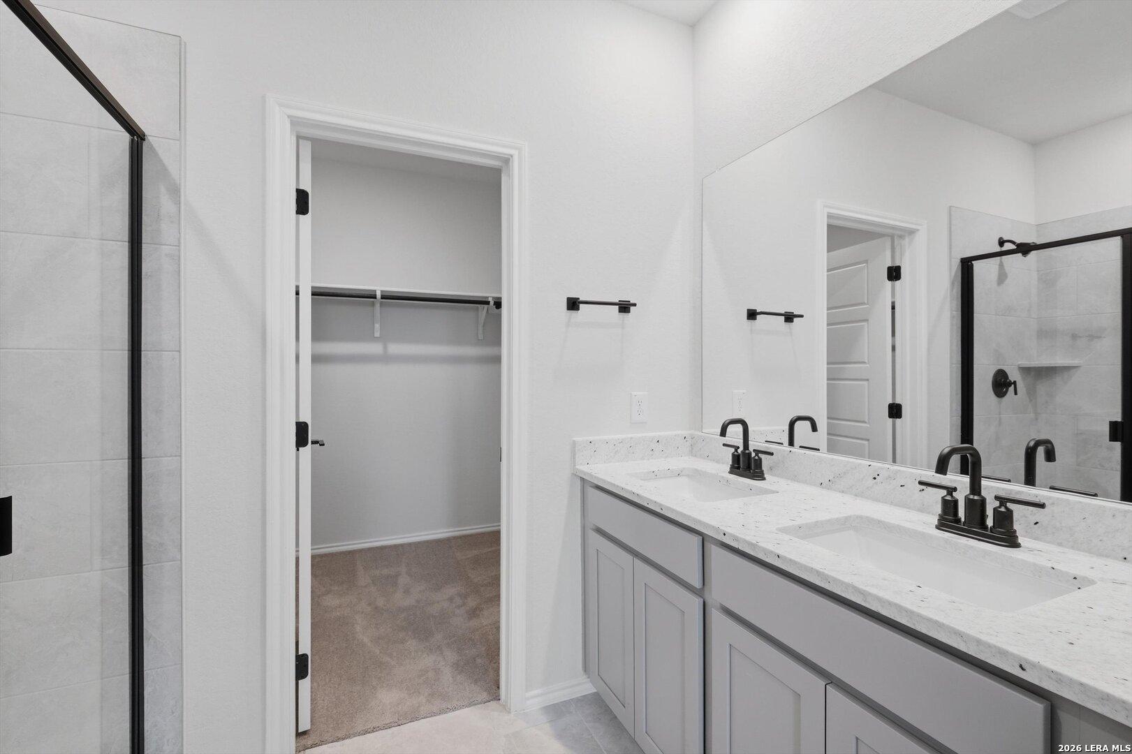 Modern master bath with double quartz vanity, gray cabinets, frameless glass shower, and adjacent walk-in closet in Davidson Homes The Blanco C, San Antonio