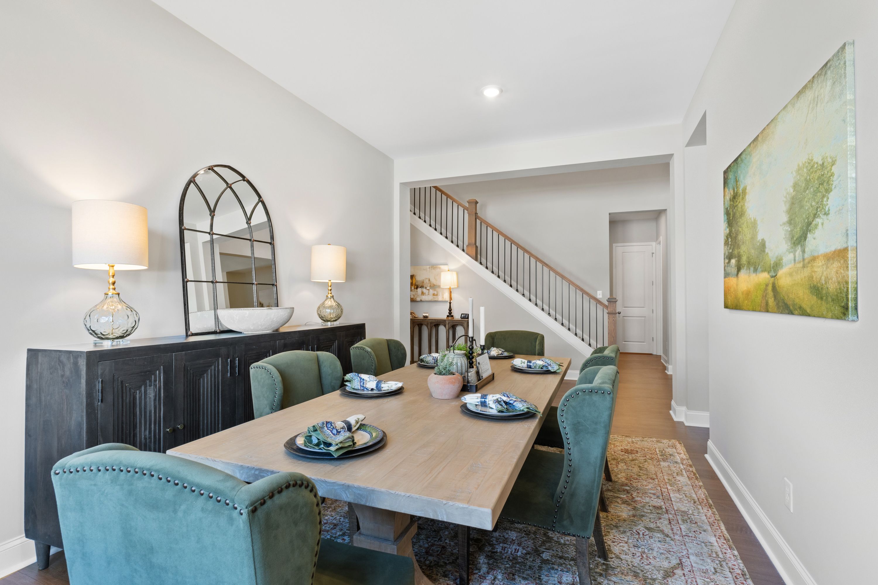 Formal dining room in The Haven D with wooden table, emerald green chairs, arched mirror, and open staircase view