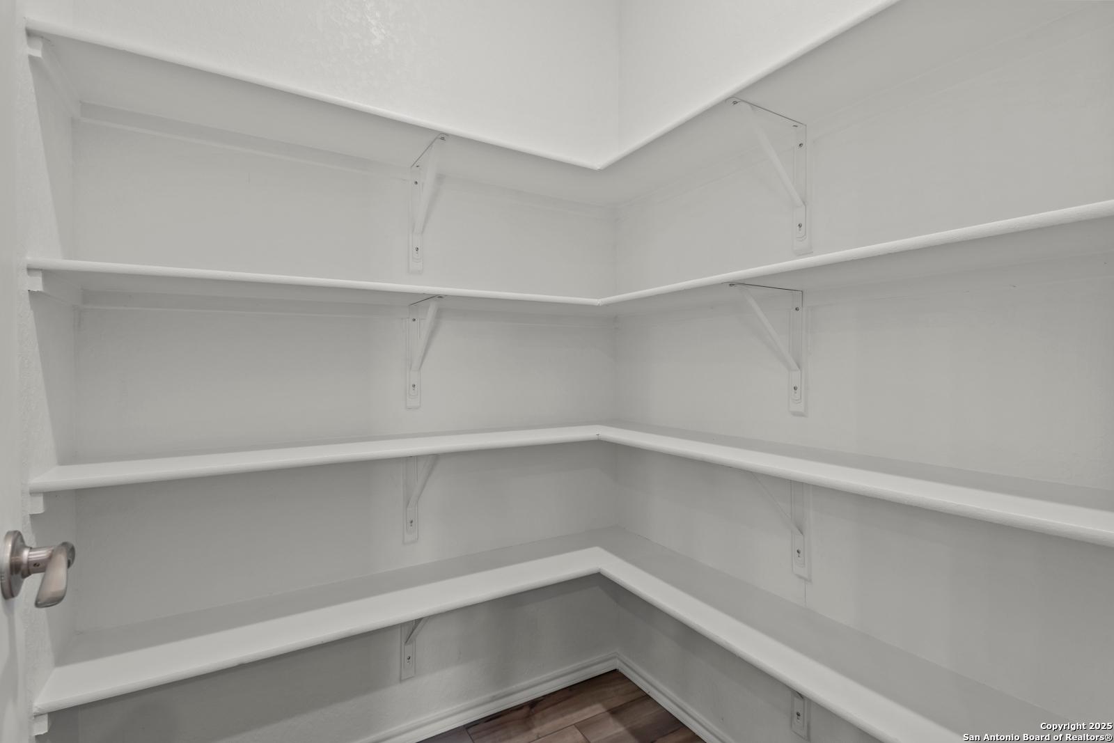 Spacious walk-in pantry with white corner shelves and hardwood floor in The Collin B 3-bedroom home, Hannah Heights, Seguin, Texas
