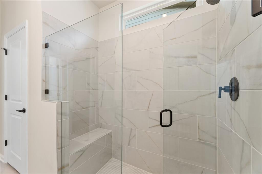 Frameless glass walk-in shower with white subway tiles, built-in bench, and matte black fixtures in The Daphne C master bath, Loganville GA