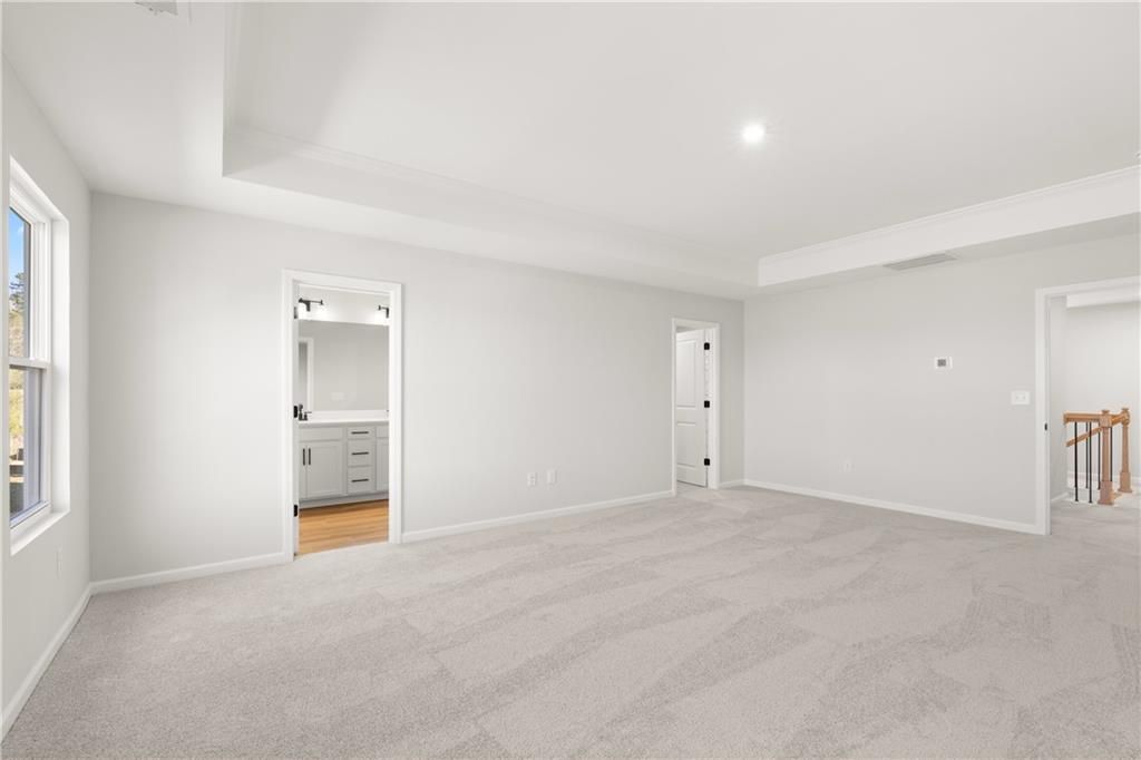 Spacious upstairs bedroom with en-suite bathroom, vanity mirror, and carpet flooring in The Cary A home, Winder, Georgia