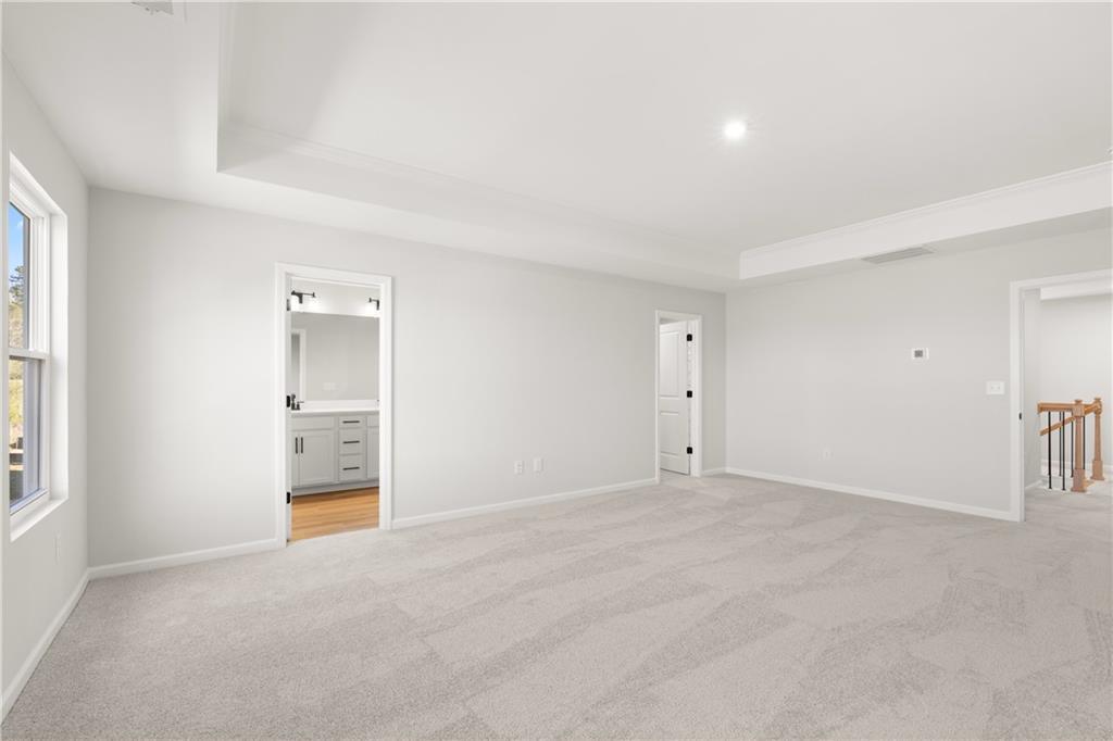 Spacious upstairs bedroom with en-suite bathroom, vanity mirror, and carpet flooring in The Cary A home, Winder, Georgia