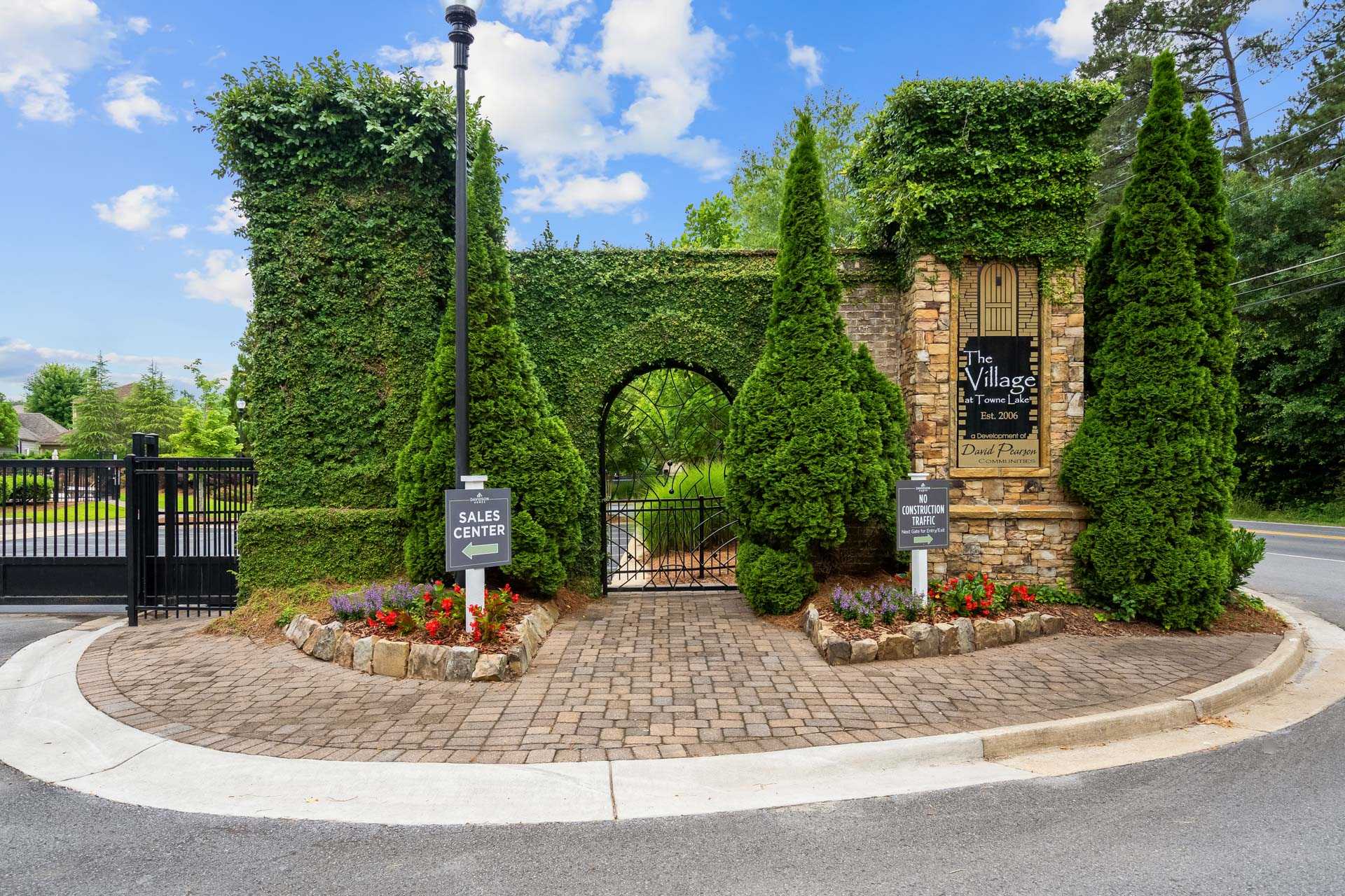 Ivy-covered stone archway entrance at The Village at Towne Lake in Woodstock GA with wrought iron gate and sales signs