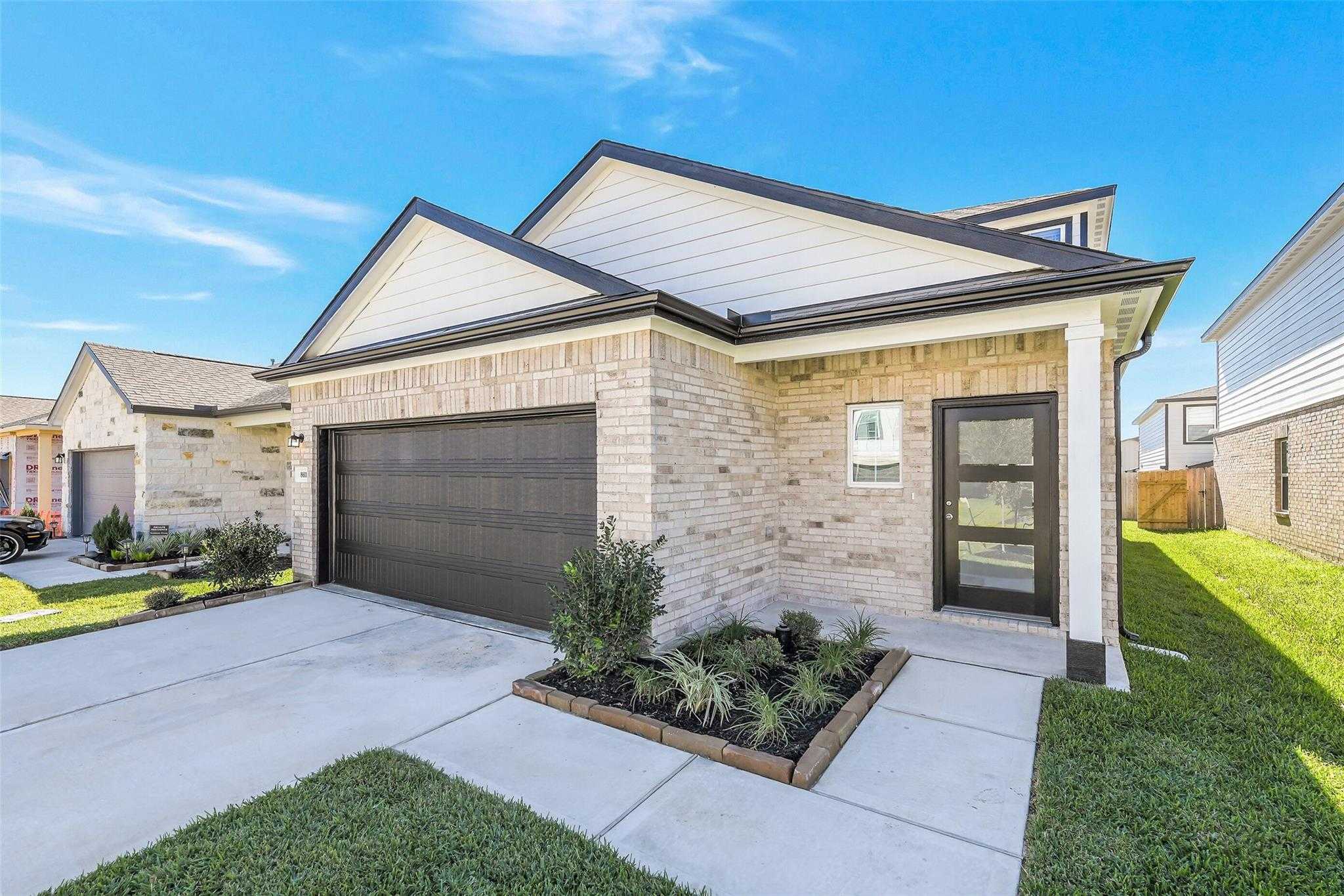 Modern 2-story brick home with 2-car garage, glass front door, and landscaped yard in Lakes at Black Oak, Magnolia, Texas