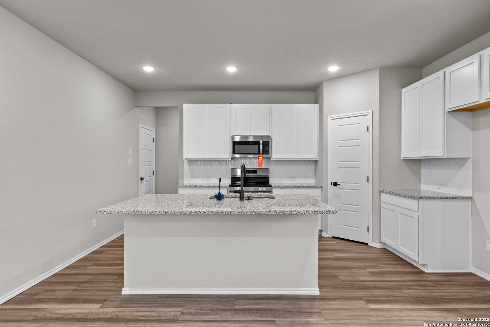 Spacious modern kitchen with granite island, white cabinets, stainless appliances in Davidson Homes The Murray I, San Antonio