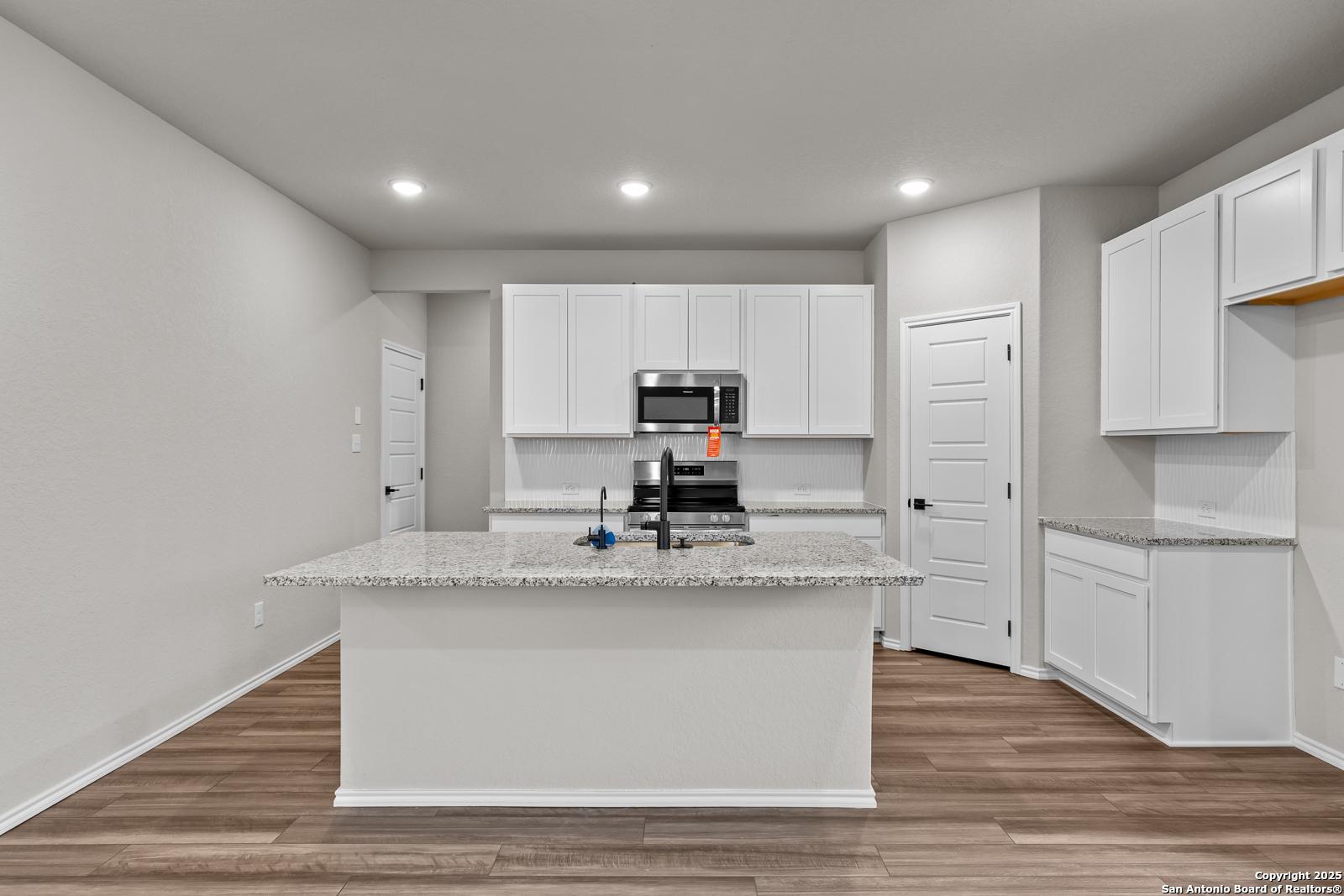 Spacious modern kitchen with granite island, white cabinets, stainless appliances in Davidson Homes The Murray I, San Antonio
