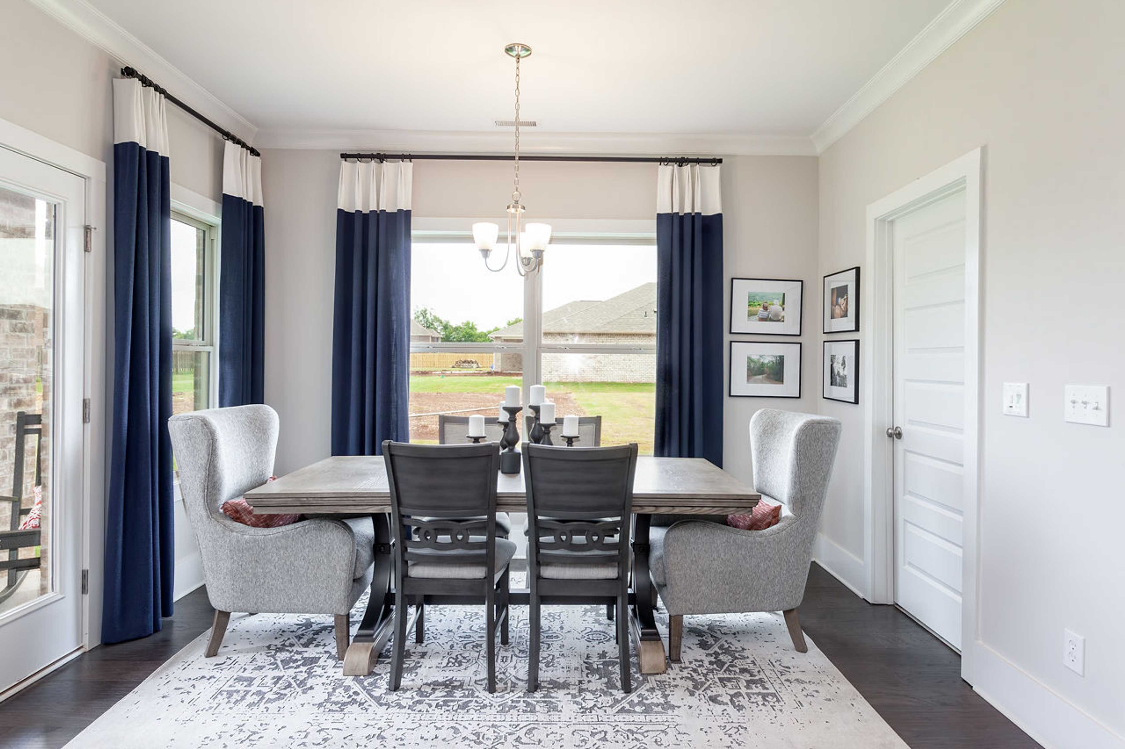 Spacious dining room at Williams Pointe in Huntsville Alabama with rustic wood table, blue curtains, chandelier, and scenic field views