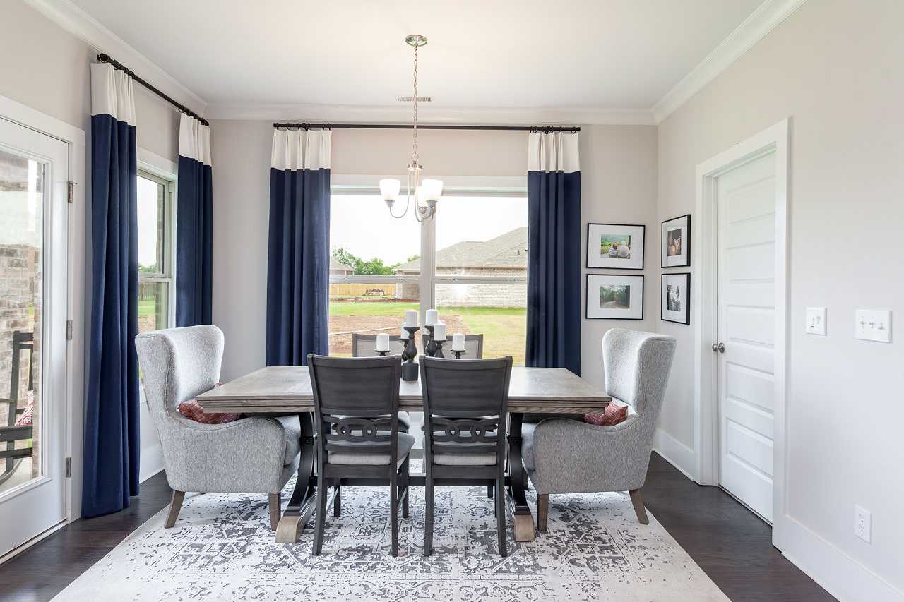 Spacious dining room at Williams Pointe in Huntsville Alabama with rustic wood table, blue curtains, chandelier, and scenic field views