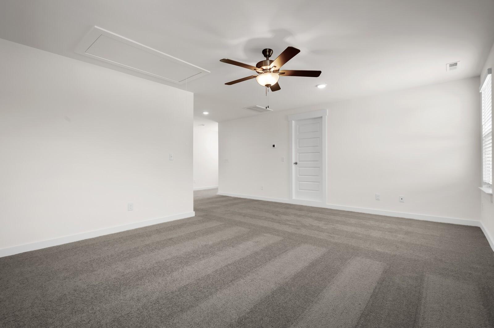 Spacious bedroom with grey carpet and ceiling fan in The Ash A floor plan at Woods Crossing, Gallatin, Tennessee.