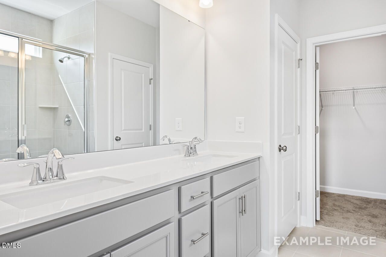 Modern master bathroom with double vanity, gray cabinets, glass shower, and walk-in closet in The Daphne C, Lillington, NC