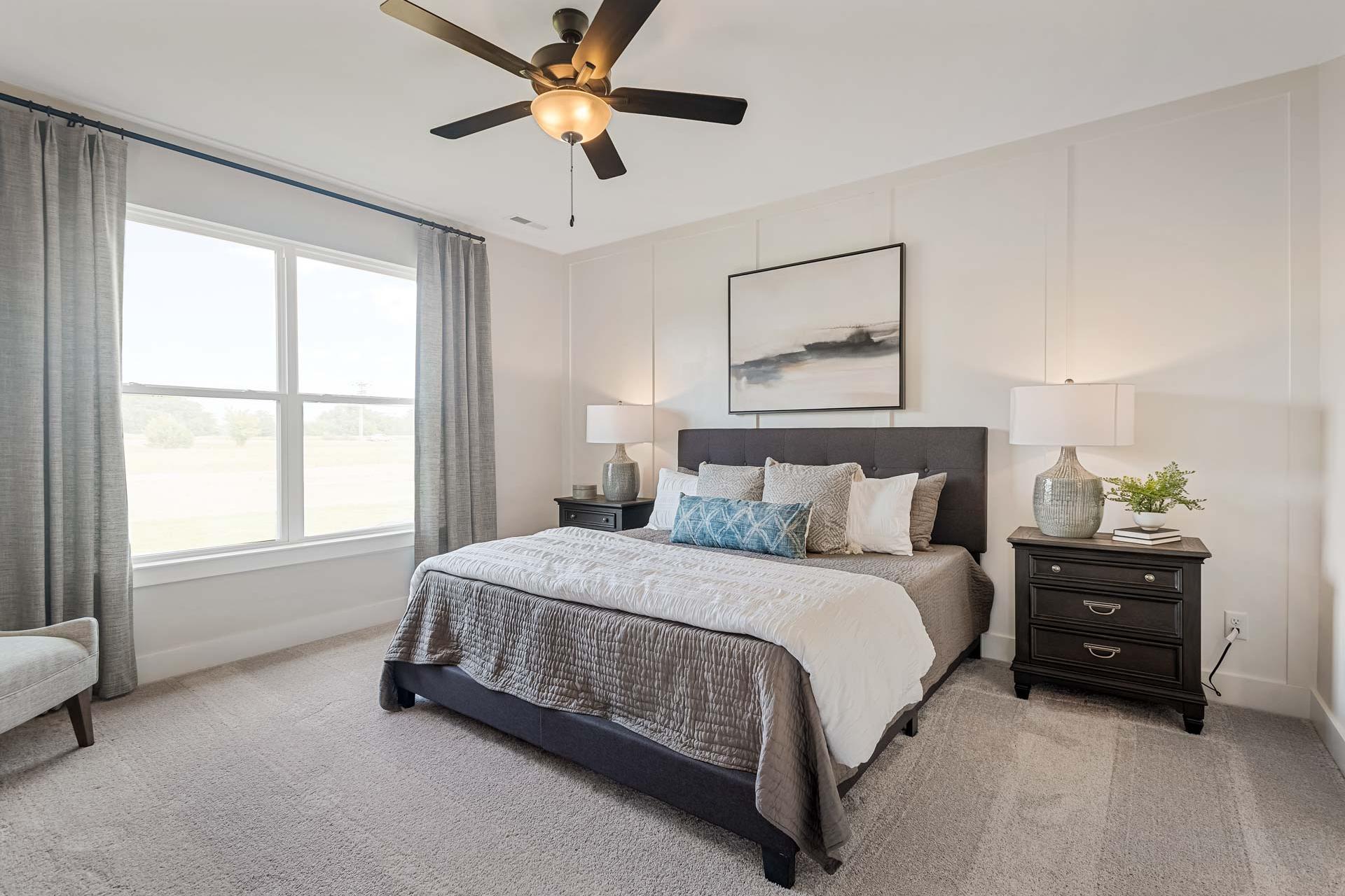 Spacious primary bedroom at Salem Landing in Murfreesboro TN featuring king bed, neutral tones, ceiling fan, and large curtained windows