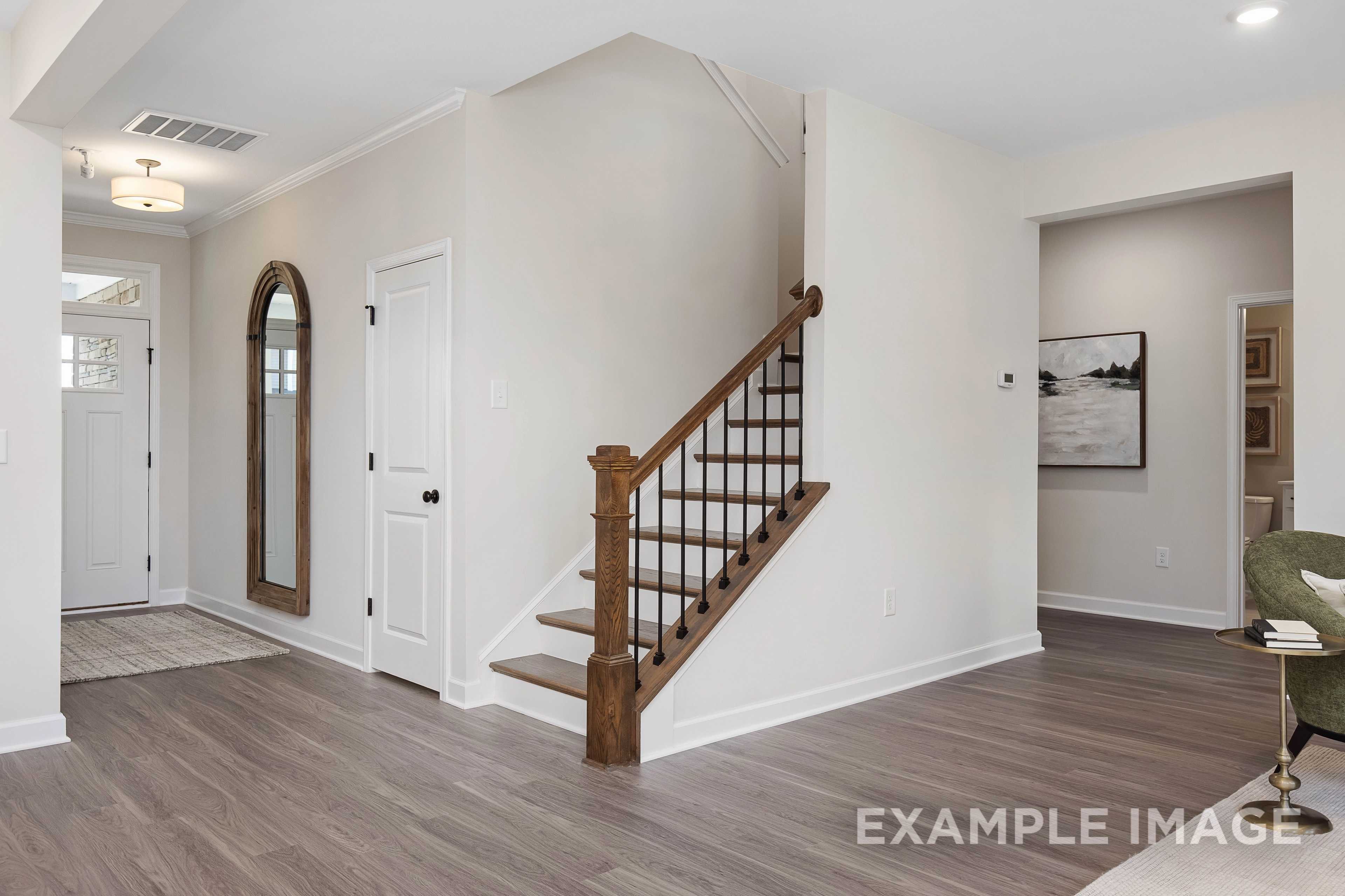 Inviting entry foyer in The Willow B 2-story home featuring wooden staircase, arched mirror, and hardwood floors, Davidson Homes Wendell NC