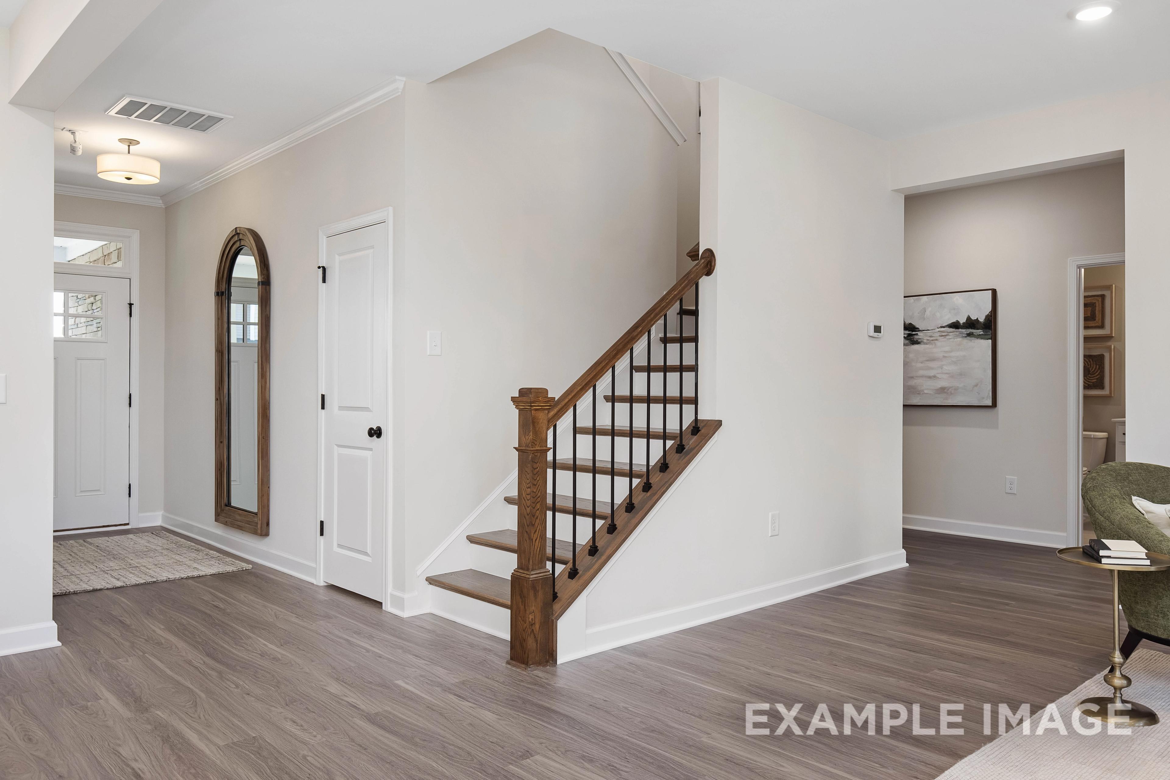 Inviting entry foyer in The Willow B 2-story home featuring wooden staircase, arched mirror, and hardwood floors, Davidson Homes Wendell NC