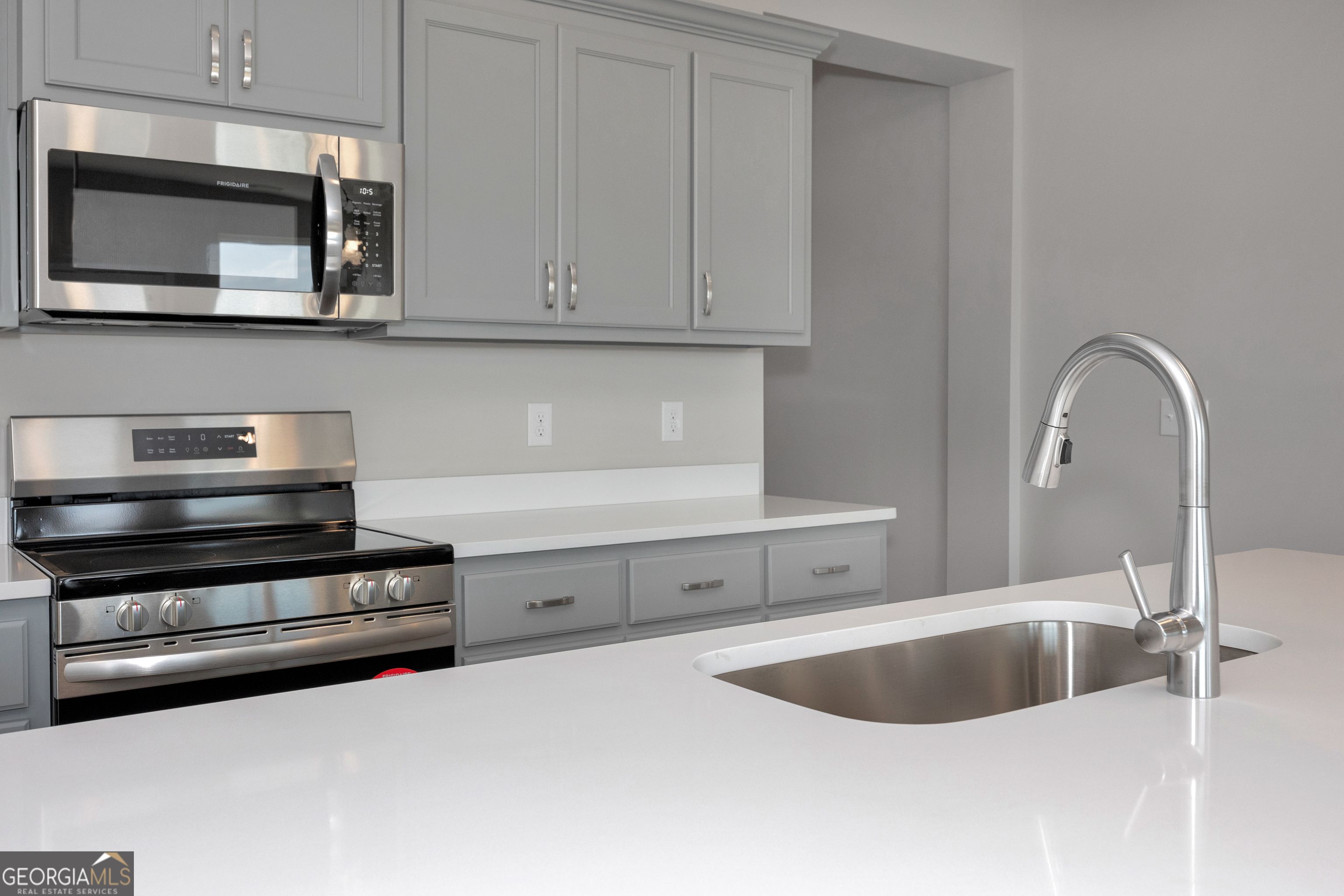 Modern kitchen featuring gray shaker cabinets, stainless steel range and microwave, white quartz counters in The Luna by Evermore Homes, Perry, GA